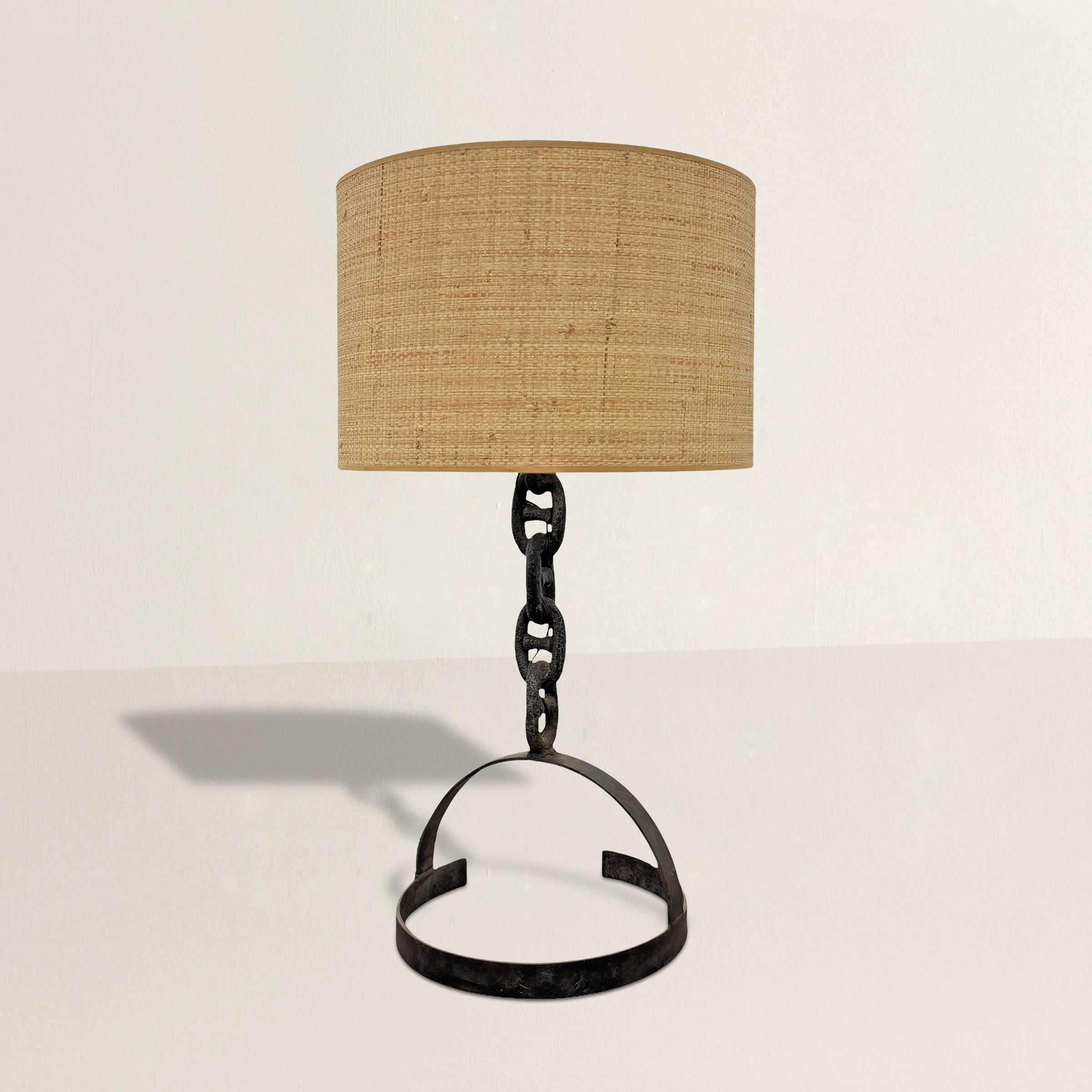 Expression audacieuse du brutalisme français du milieu du XXe siècle, cette lampe de table frappante est fabriquée à partir d'une chaîne en fer de gros calibre, sa force industrielle étant adoucie par l'ajout d'un abat-jour en raphia. La forme