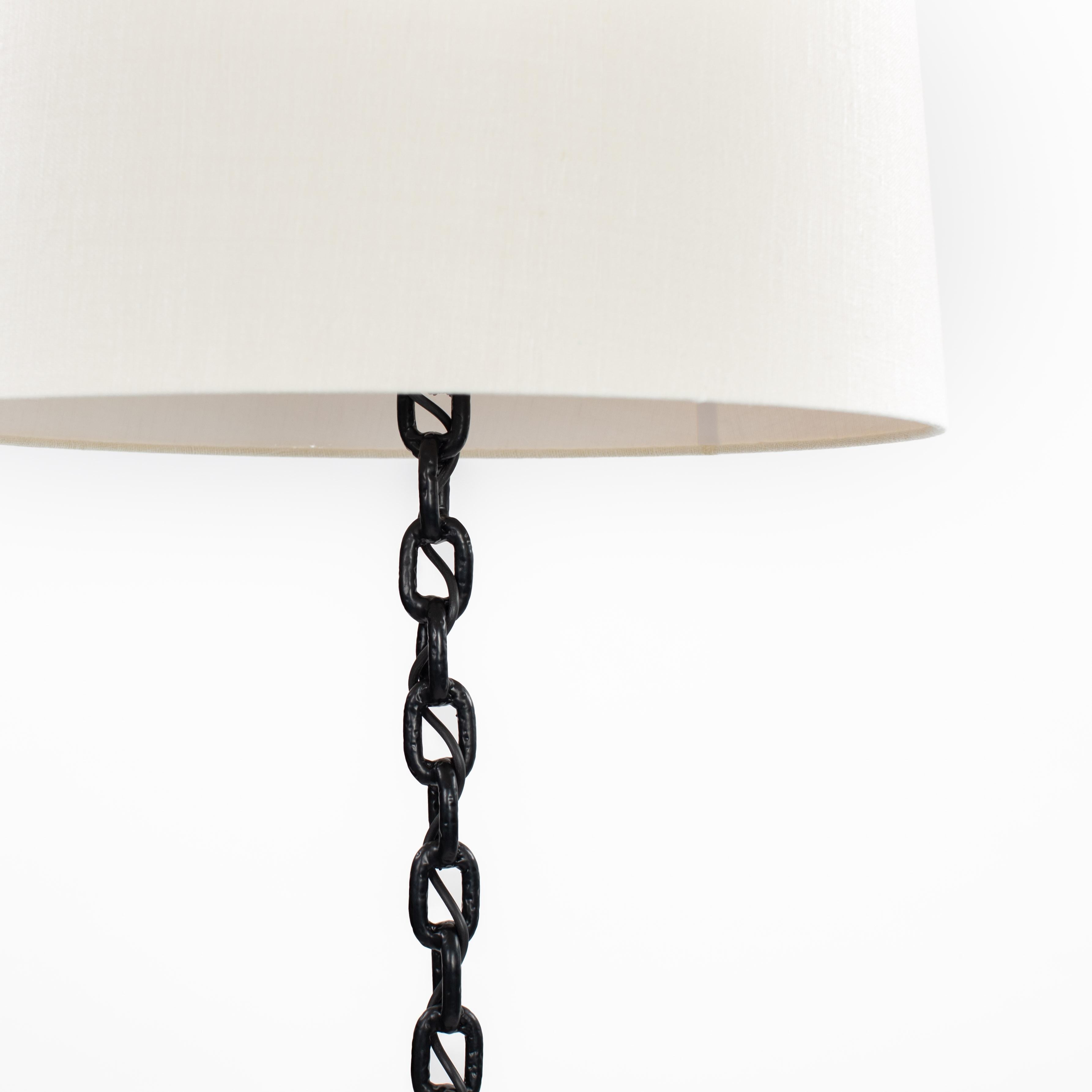French Brutalist Mid-Century Black Iron Chain Floor Lamp White Silk Shade 1960s.

The lamp is a real eye-catcher.
The chain links are forged together lengthwise to form the long lamp base, which runs out on 3 sweeping legs that tilt upwards at the