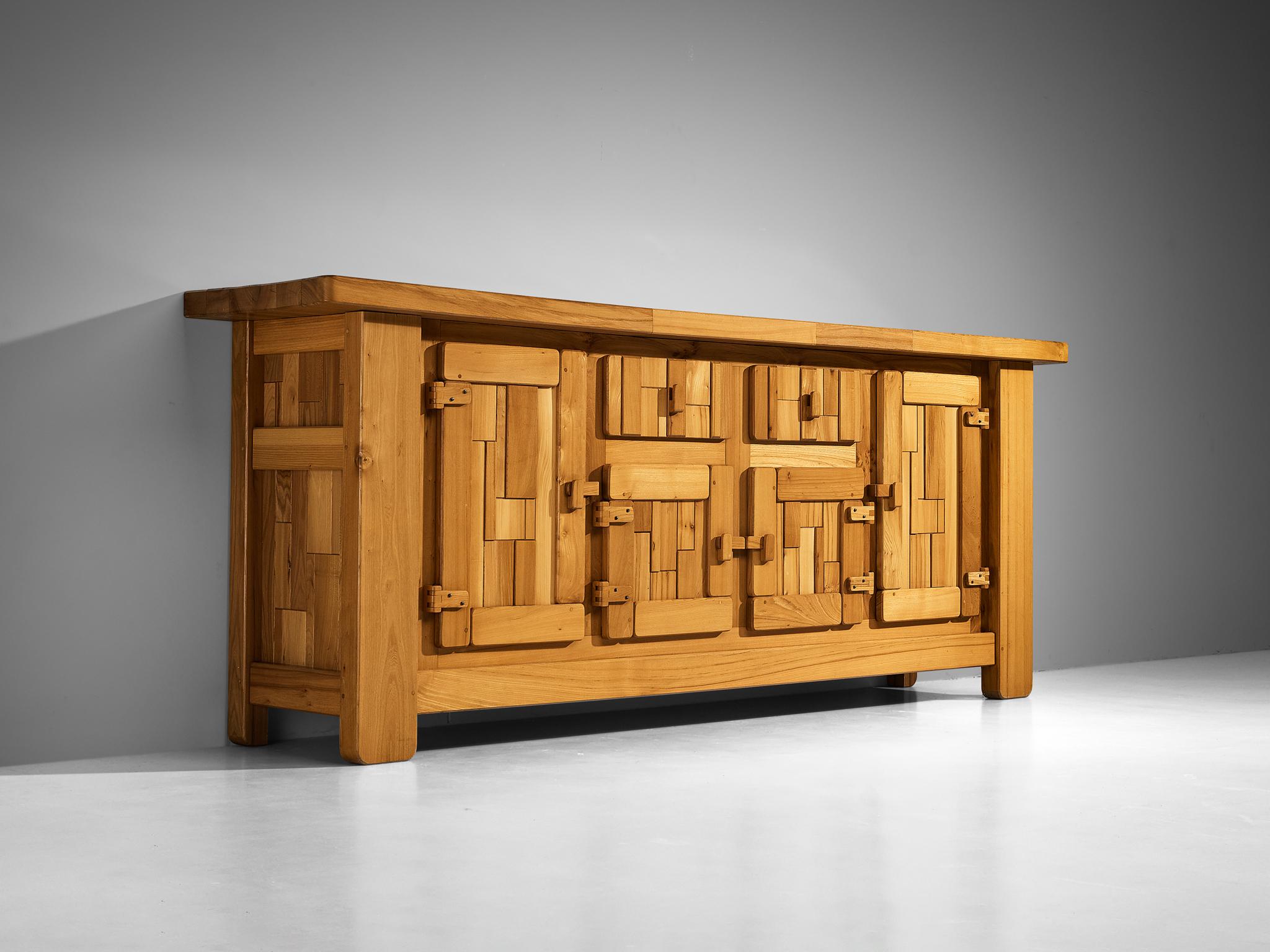 Sideboard, solid elm, France, 1970s

This sideboard exemplifies exceptional woodworking, highlighted by its graphically designed doors that create a dynamic and tactile rhythm across the front. Each door panel features an asymmetrical arrangement of