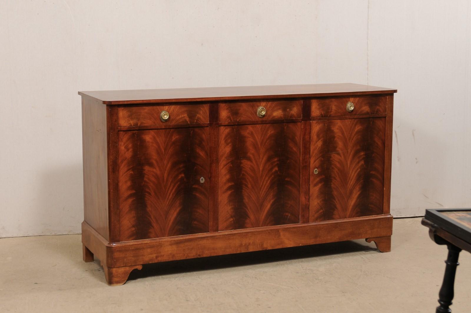 A French mahogany buffet cabinet from the mid 20th century. This mid-century French sideboard, just over 6 feet in length, is covered in a gorgeous fire-grain mahogany veneer. This case-piece houses three drawers along the top with three doors set
