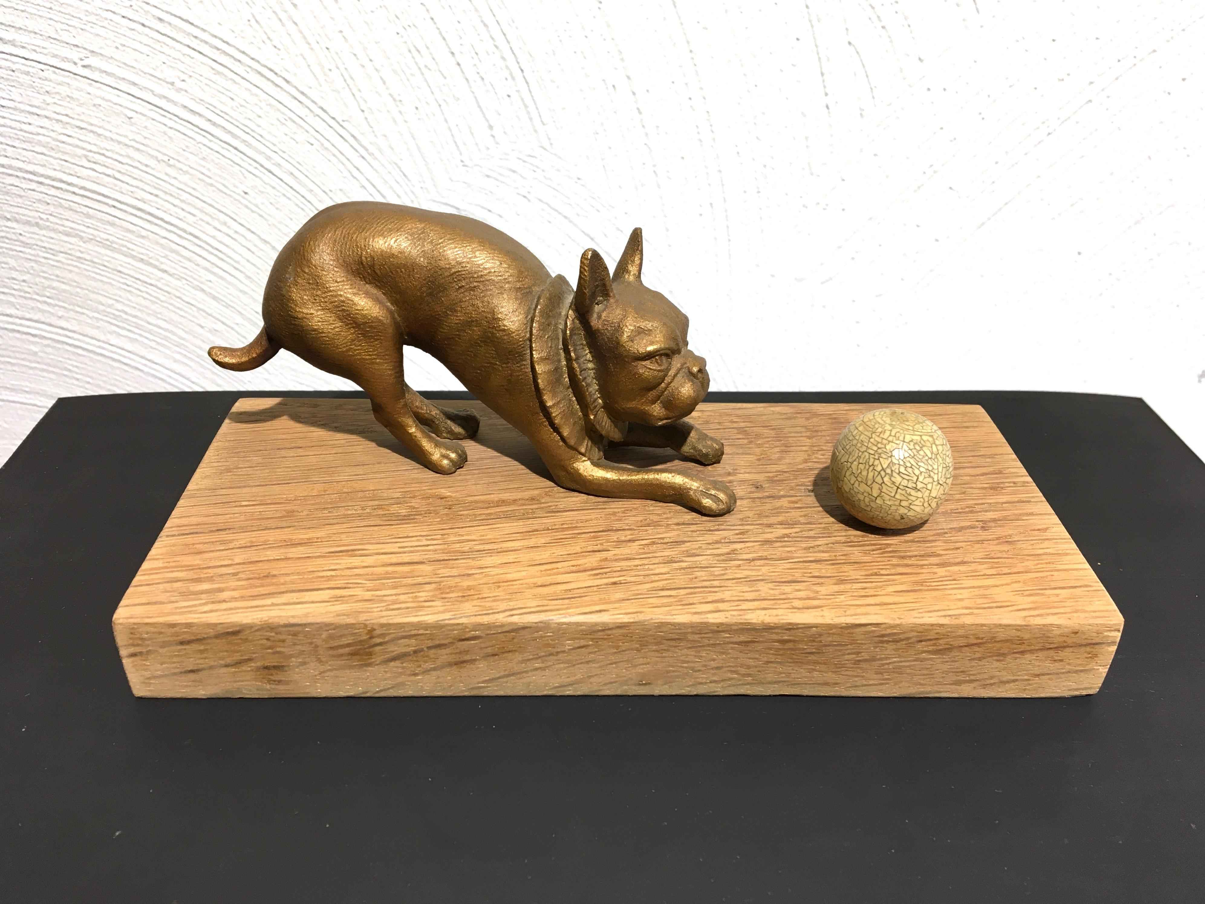French bulldog playing with ball sculpture. 
A gold painted metal bulldog sculpture with ball mounted on a wooden base. 
The bulldog sculpture is very detailled , look at his head, eyes, nose, paws and beautiful collar around his neck.  In the
