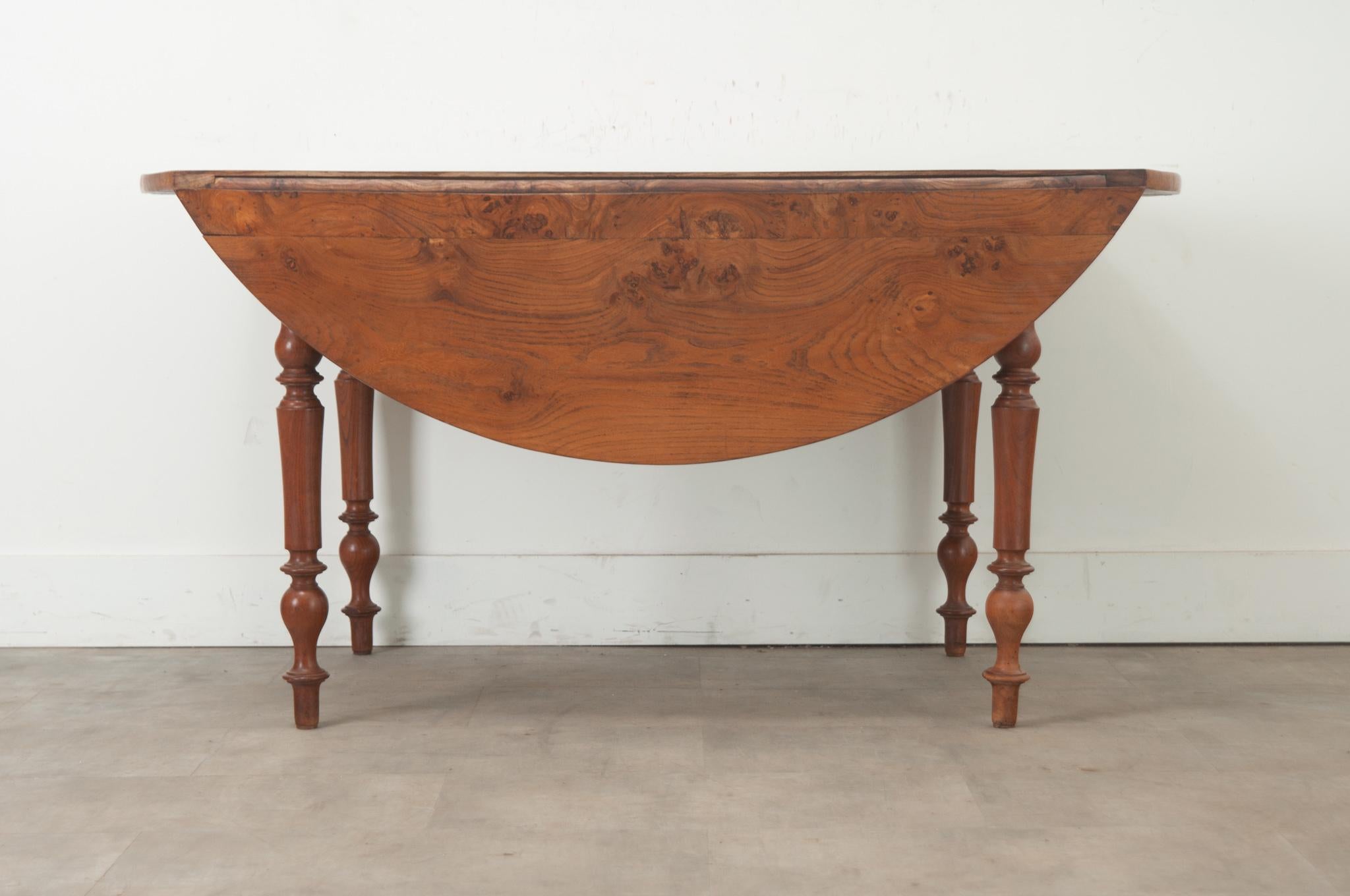 This versatile French drop leaf table is made of burl fruitwood and can be used as a console or a dining table. The top sits over four turned legs which add character to this classic dining table. The drop leaves are supported with slides that are