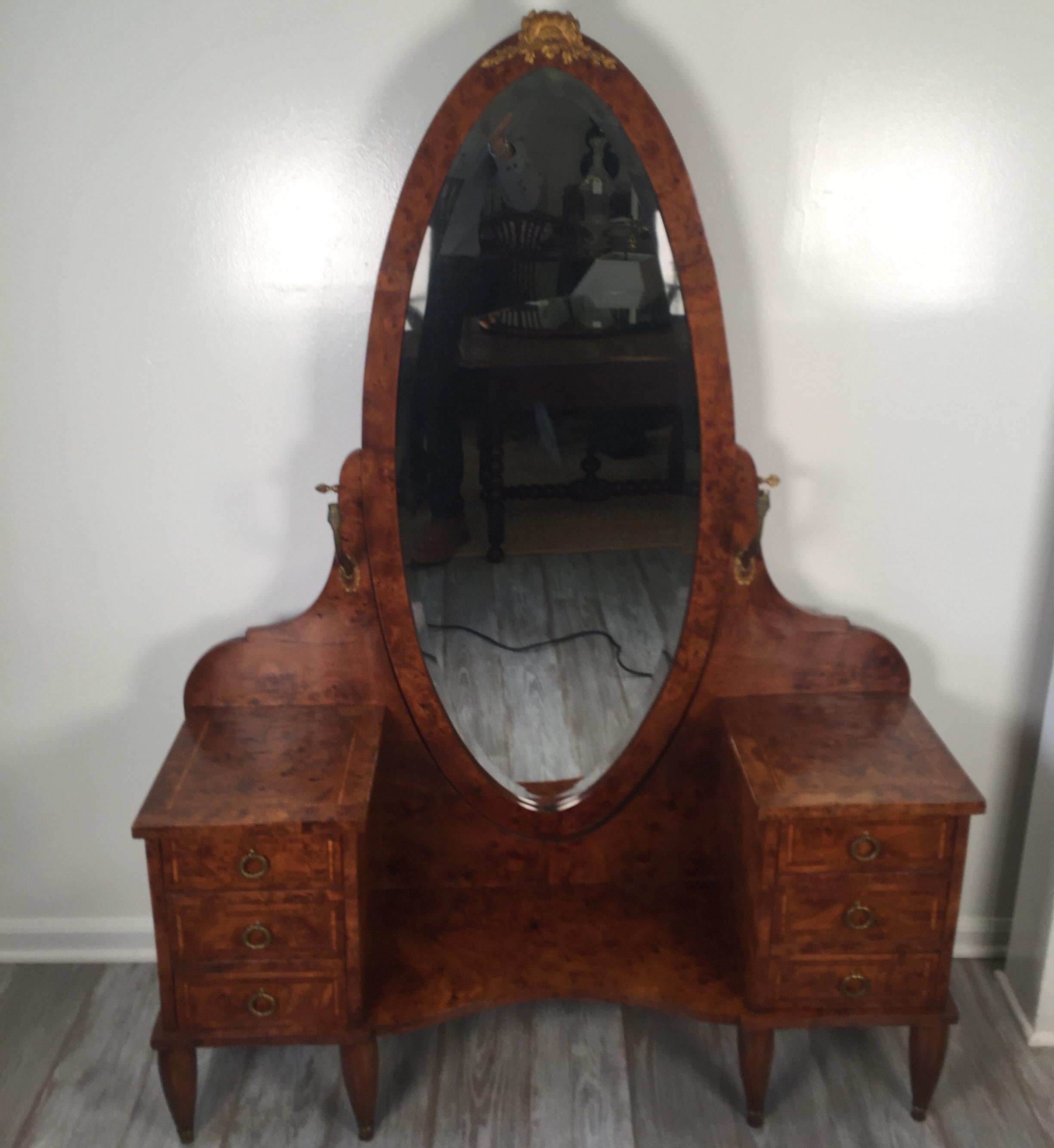 Graceful French burled walnut vanity with dramatic oval mirror. Three drawers on each side with gilt bronze ring handles. The beveled mirror with ormolu mount on top with a pair of small mounted electrified sconces one on each side.