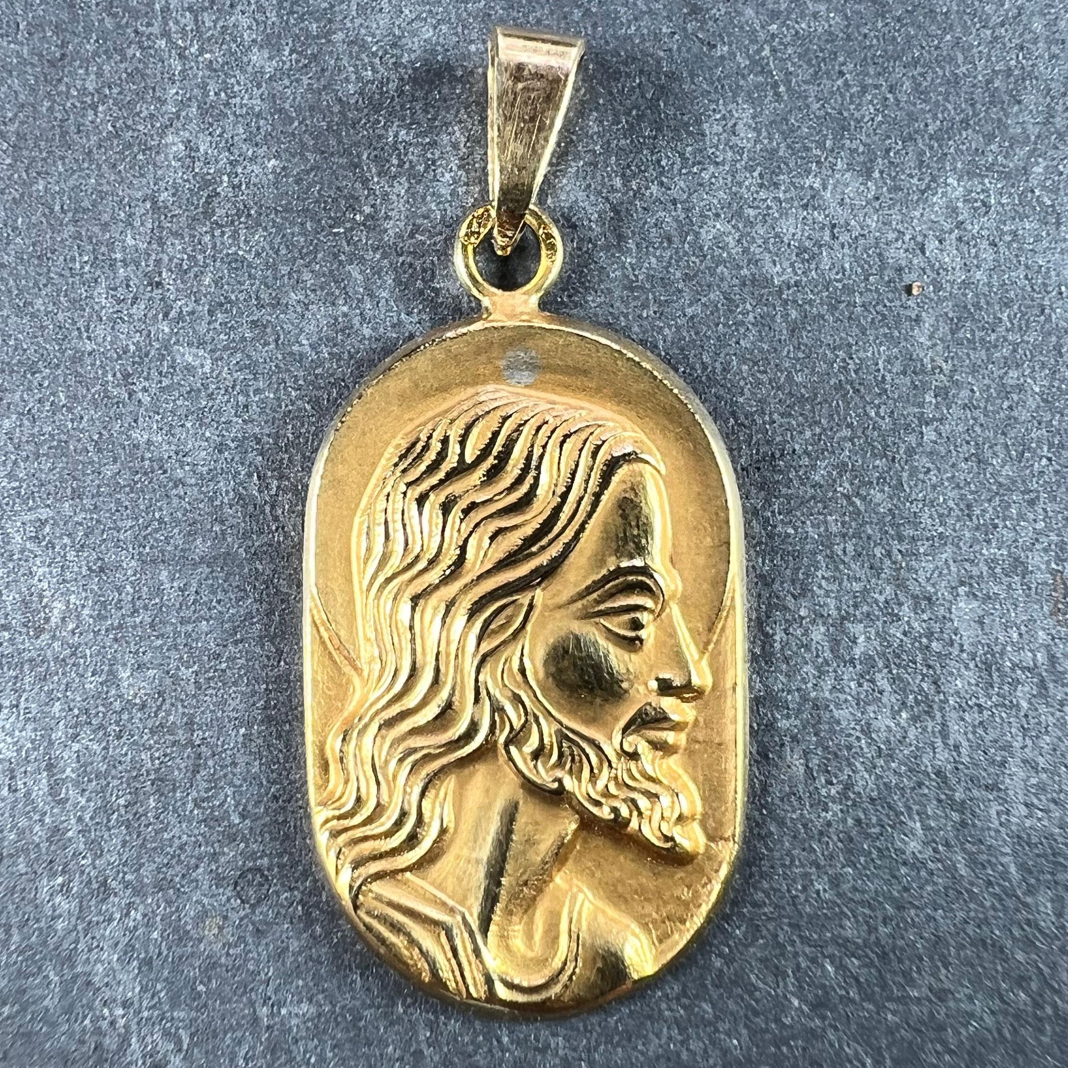 A French 18 karat (18K) yellow gold charm pendant designed as an oblong medal depicting Jesus Christ in profile with a halo. Signed Butsch, stamped with the eagle’s head for 18 karat gold and French manufacture, along with an unknown maker's mark,
