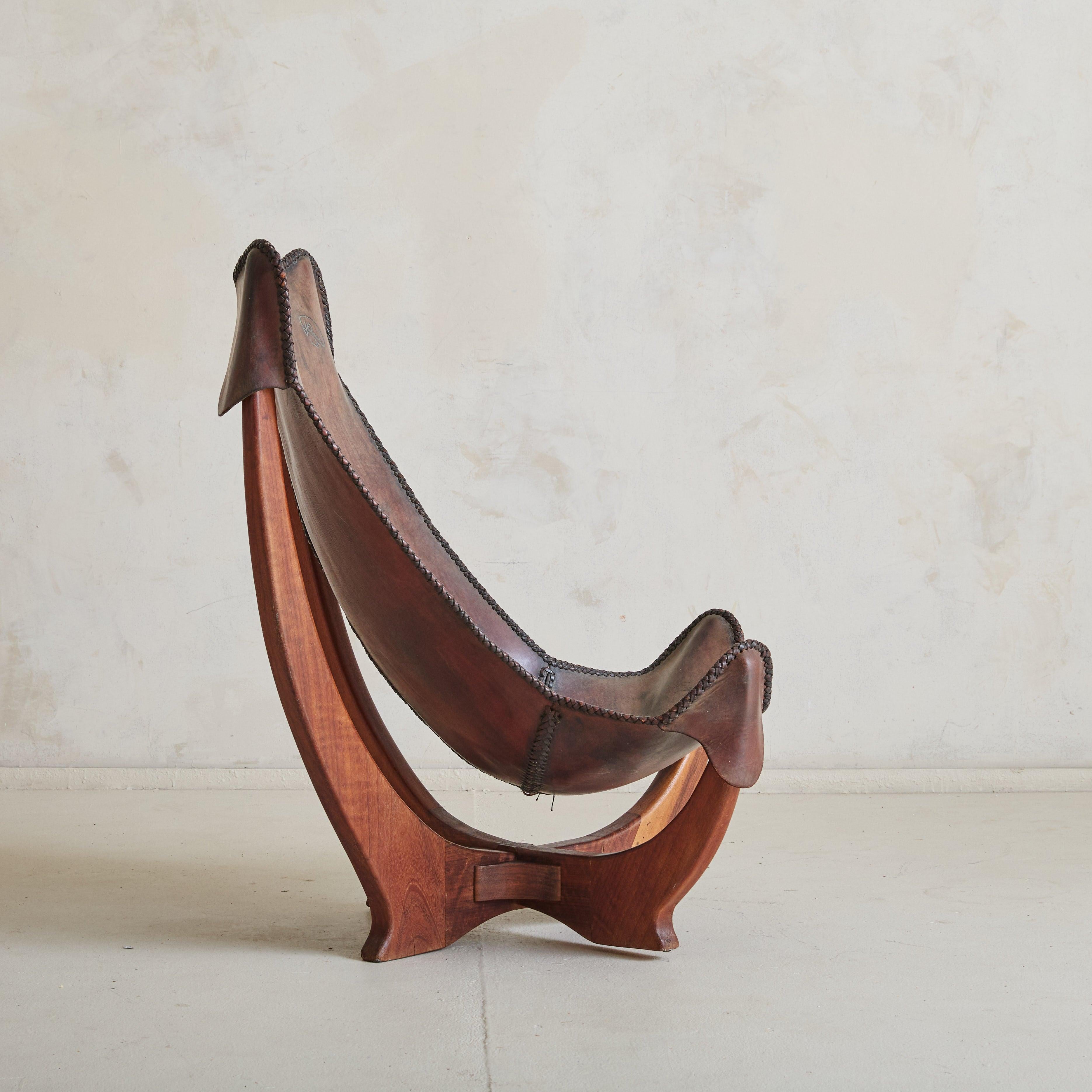 A rare butterfly lounge chair, handcrafted by a French artisan in the 1960s. This one-of-a-kind piece features a natural cowhide leather seat supported by an architectural solid wood frame. The saddle-stitched brown leather, rich with patina,