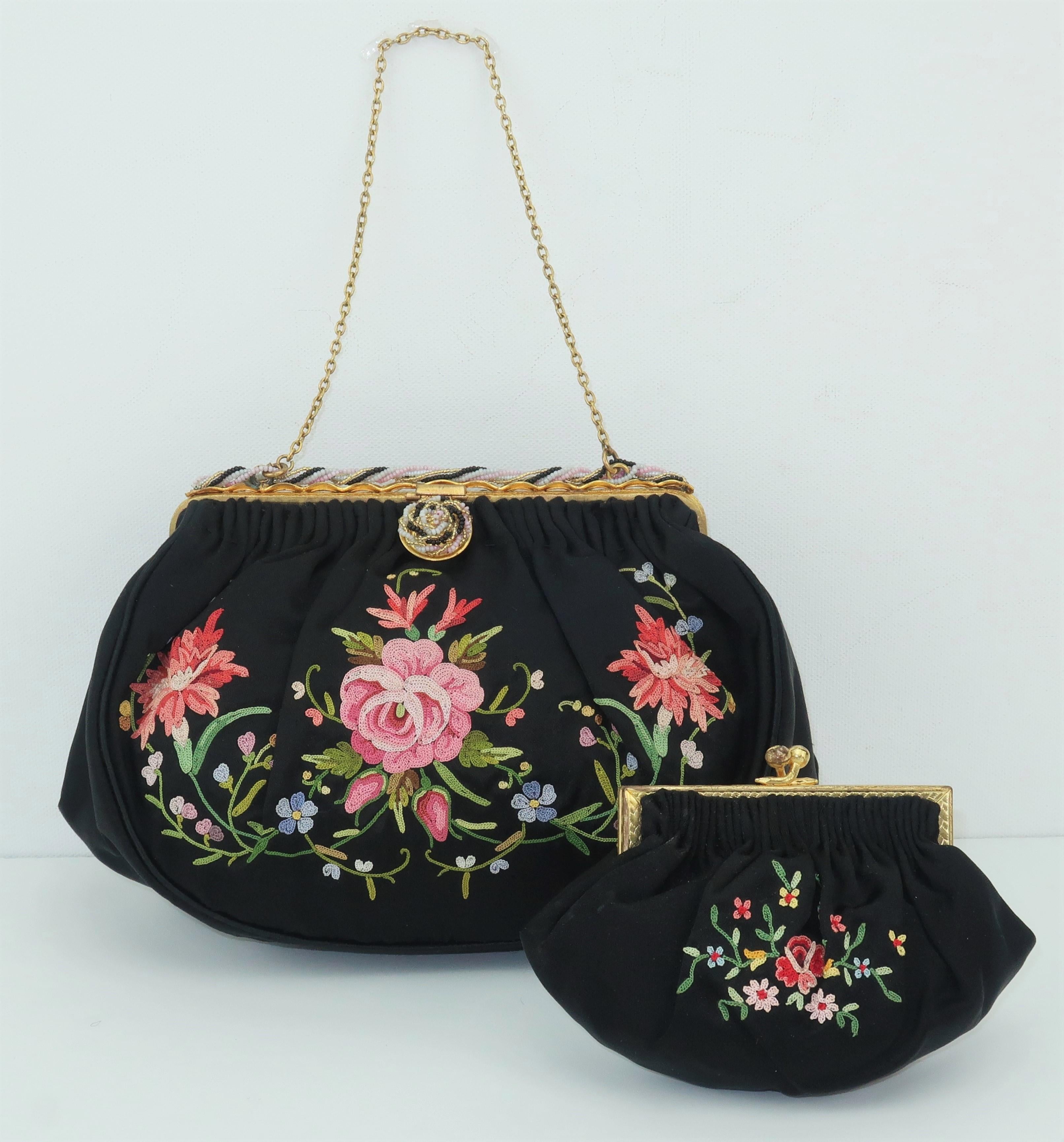 This delicate and ultra feminine C.1950 French black satin handbag features a bright floral chain stitch pattern in shades of pink, red, yellow, blue and green and a chain handle. The gilt metal frame is accented by a braided seed bead design with a