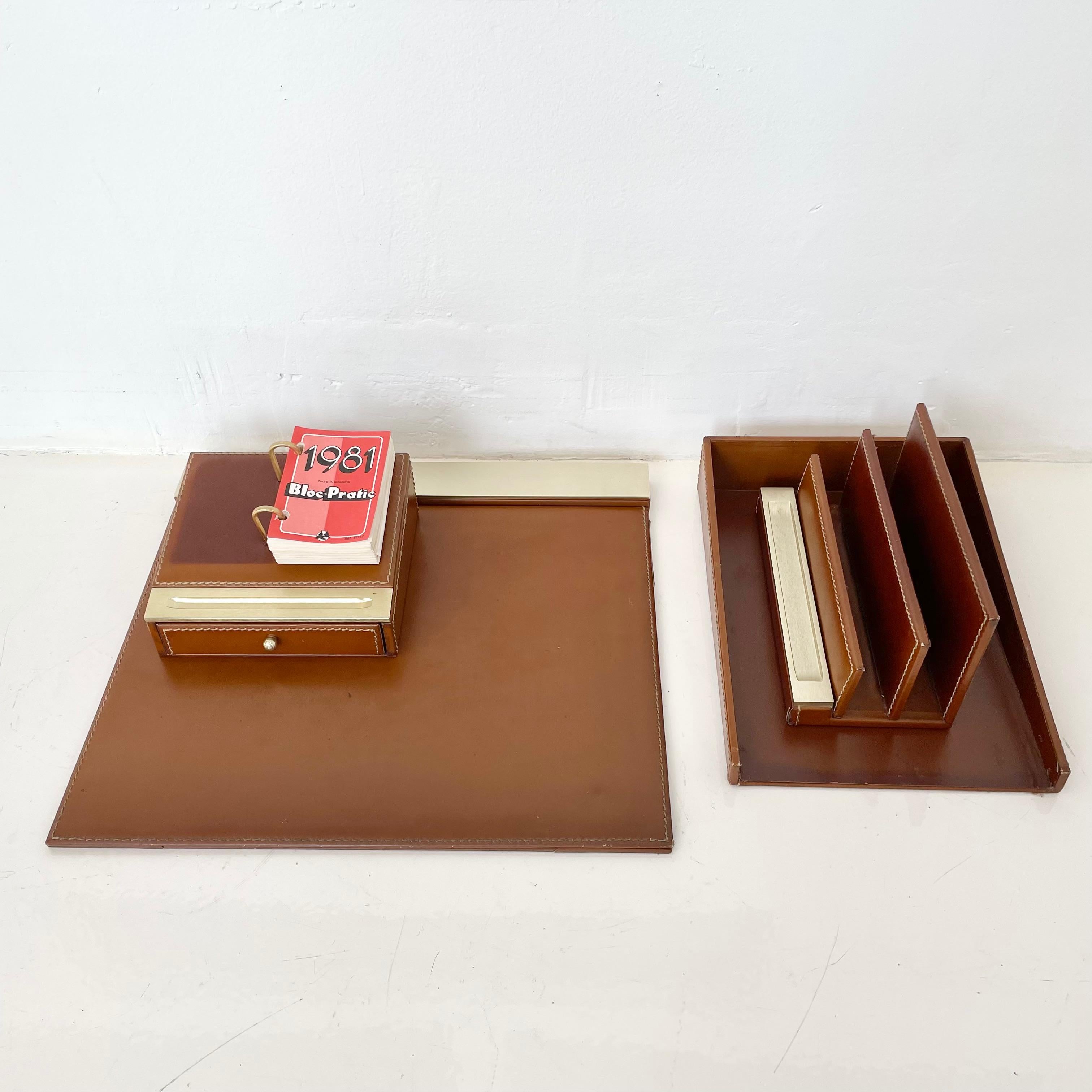 Fantastic 4-piece French leather desk set by Le Tanneur. All pieces wrapped in camel leather. Desk set includes: desk pad, mail holder, paper tray, and calendar holder. Brass trim on three of the four pieces. Two small pull out drawers underneath