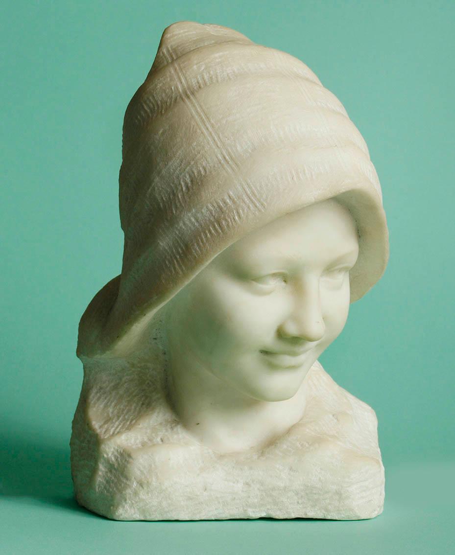 Beautiful serene bust of a young girl with a hat on her head. She has a beautiful glow on her face.
The statue is carved from Carrara marble and has a beautiful antique patina. The image is not signed. It was probably made circa 1920-1930 in France.