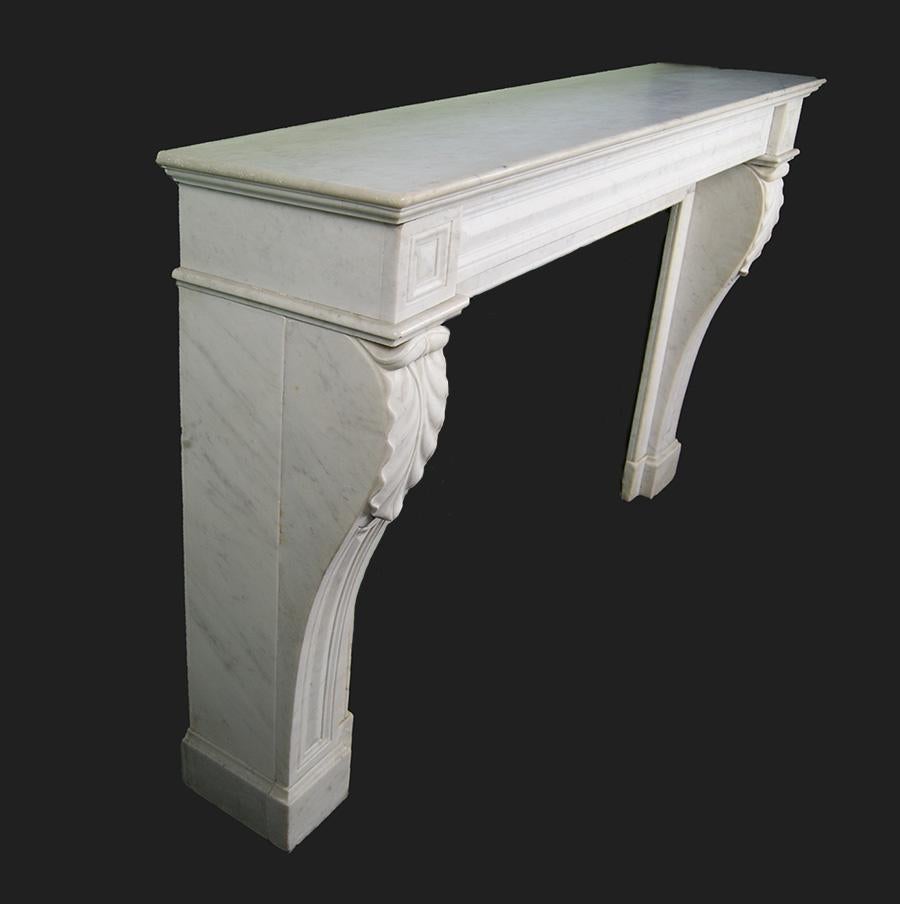 Cheminée française en marbre de Carrare de bonne qualité et de forme Louis XVI. Les montants de la console à panneaux sur plinthe sont ornés d'un décor d'acanthe stylisé. La frise simple à panneaux est flanquée de blocs d'angle sous un important