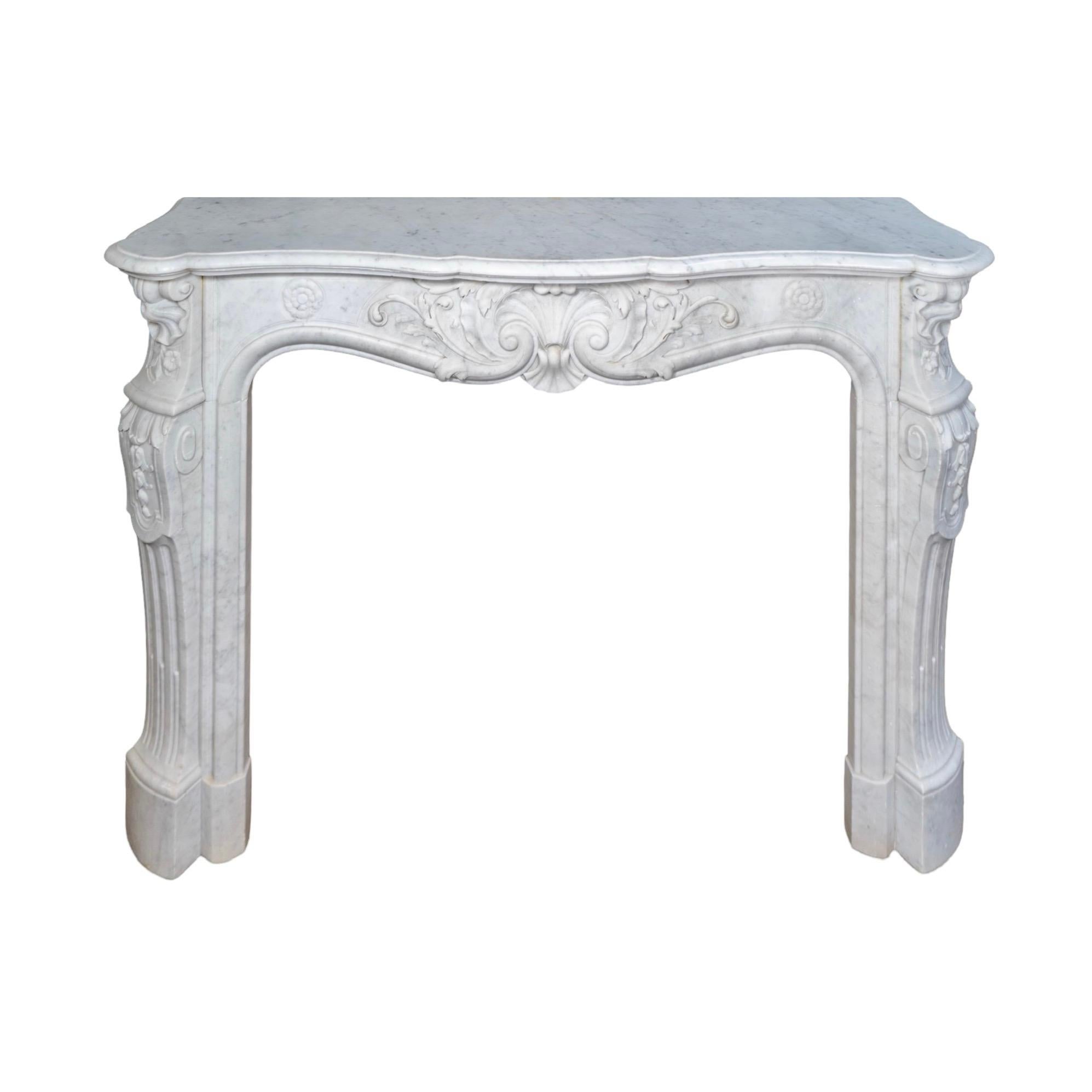 Cette cheminée française du XIXe siècle, réalisée en marbre de Carrare veiné de blanc, est une étonnante pièce ancienne récupérée. Ses détails sculptés de manière complexe sont mis en valeur par un motif central de fleurs et de coquillages, avec de