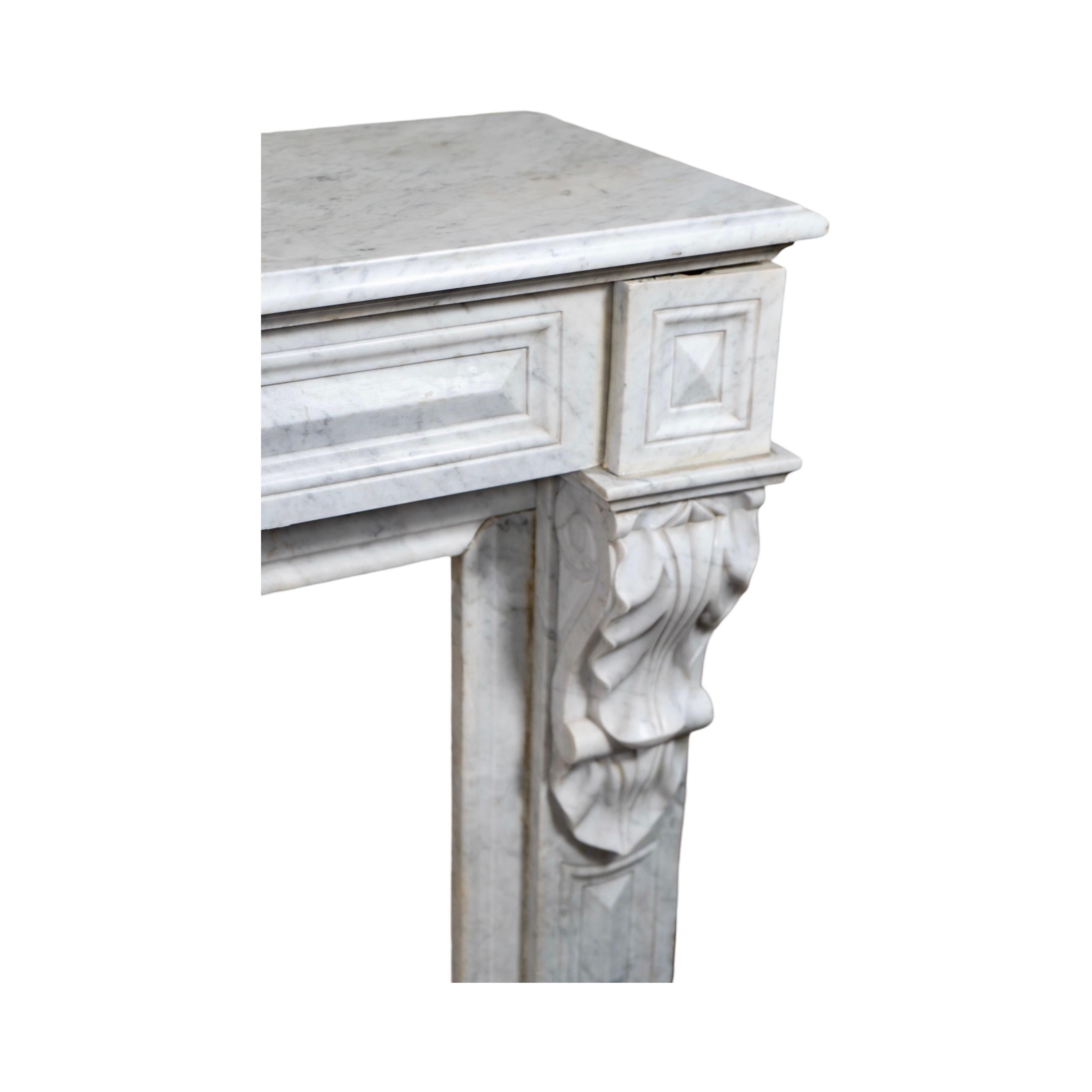 Una antigua repisa de mármol de Carrara veteada en blanco, que data de la década de 1890 y fue tallada a mano en Francia. La pieza central presenta tallas geométricas triangulares en la clave, mientras que motivos geométricos cuadrados adornan la