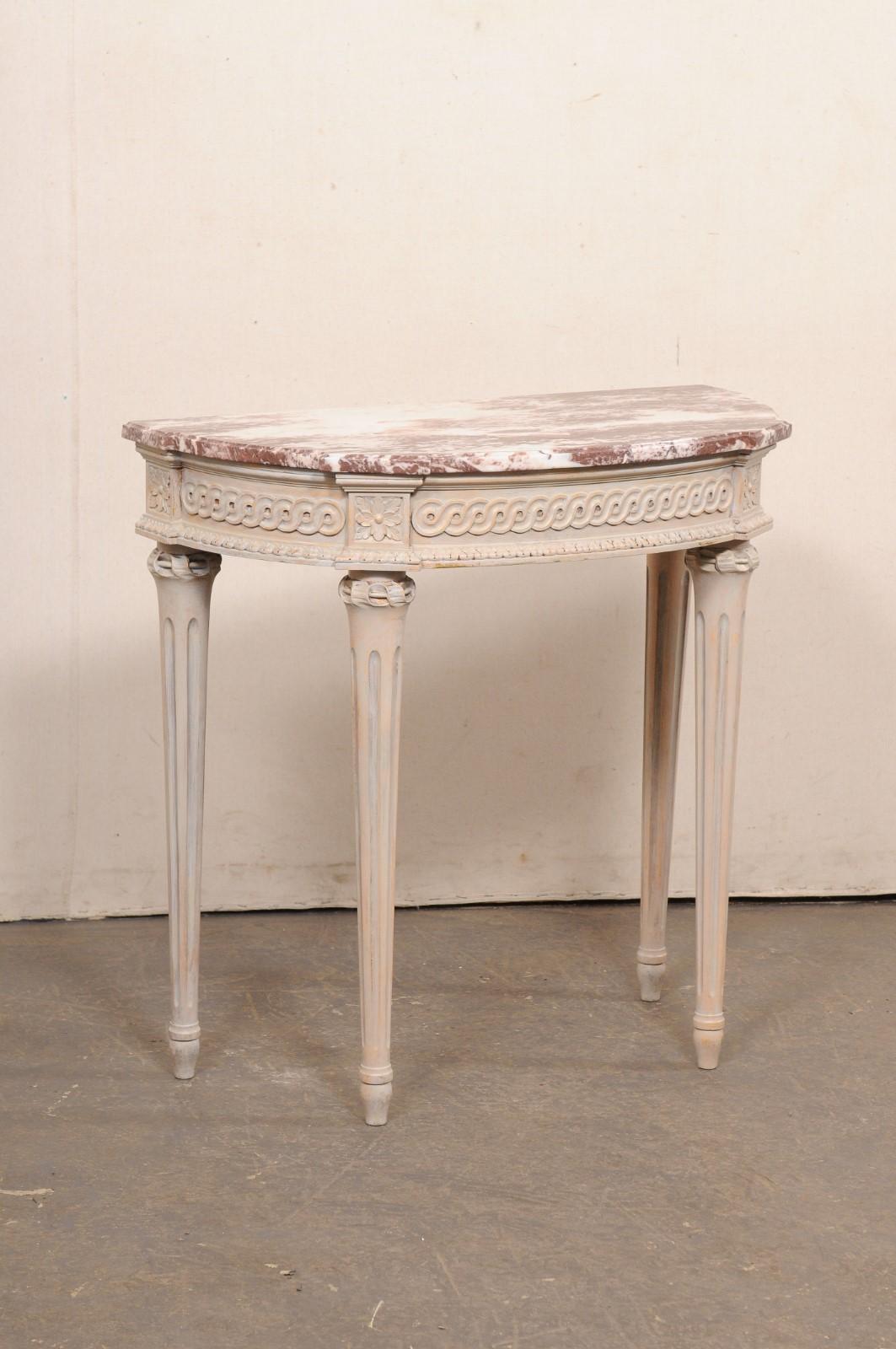 A small-sized French carved and painted console table with marble top. This vintage table from France has a marble top (D-shaped with accentuated projections at either front corner and rear corners), which rests above the apron which has been