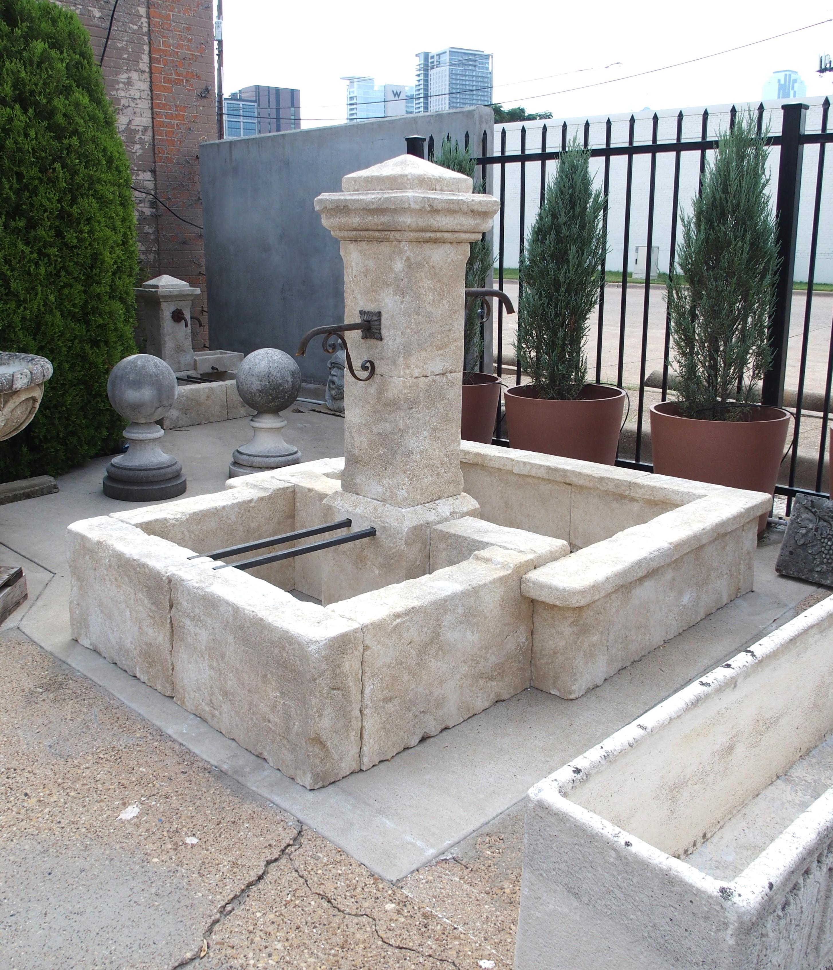 Cette fontaine centrale en pierre calcaire sculptée à la main, originaire de Provence, en France, comporte deux bassins rectilignes de tailles différentes, flanqués d'un seul pilier. Une paire de becs en fer à volutes émanent de la colonne centrale,