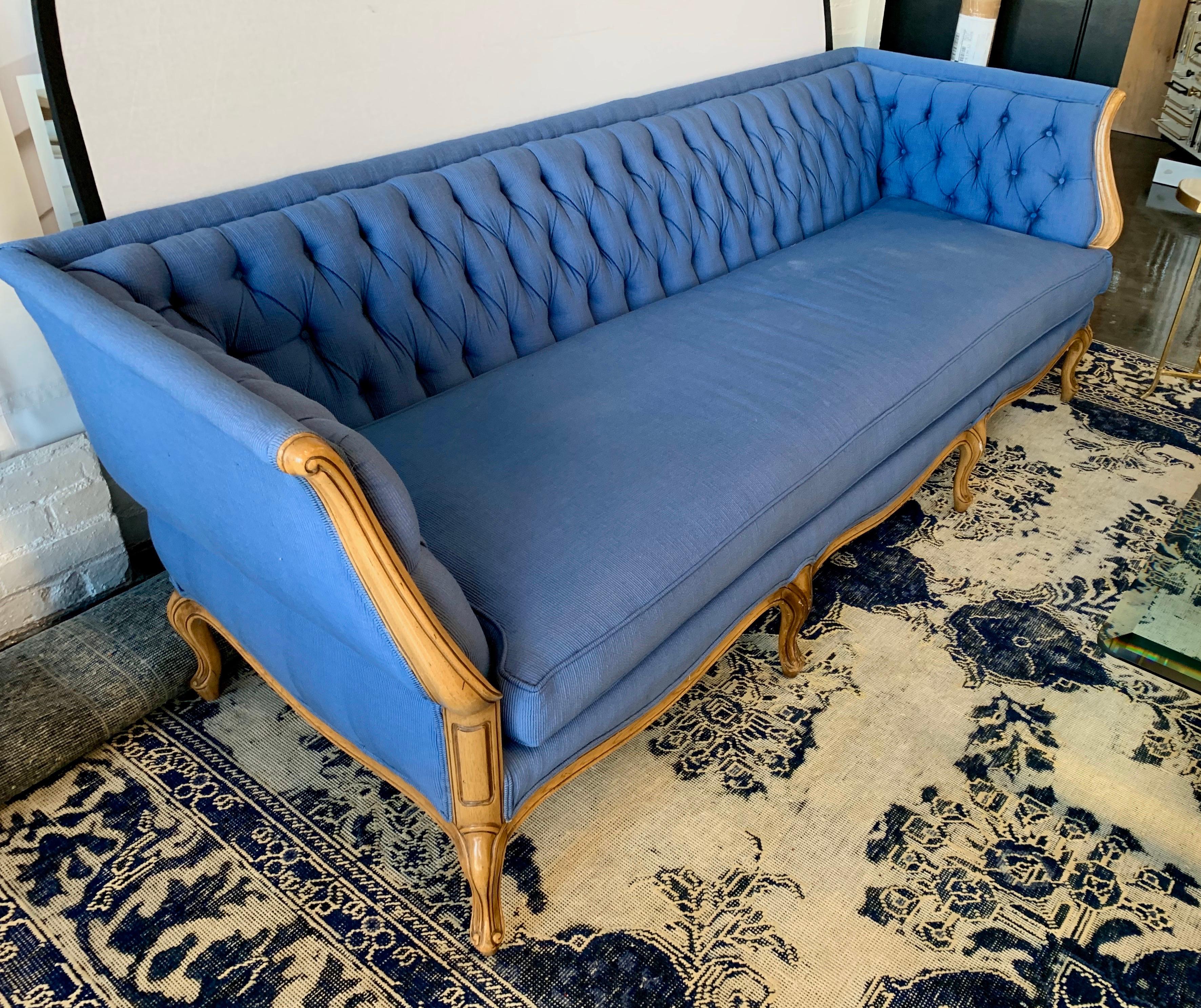 A beautiful vintage tufted sofa with a carved fruit wood frame. Tufted on back and inside arms. Newer cotton upholstery in the Pantone blue color of 2020. It has a subtle raised ribbed pattern. Down seat cushion.