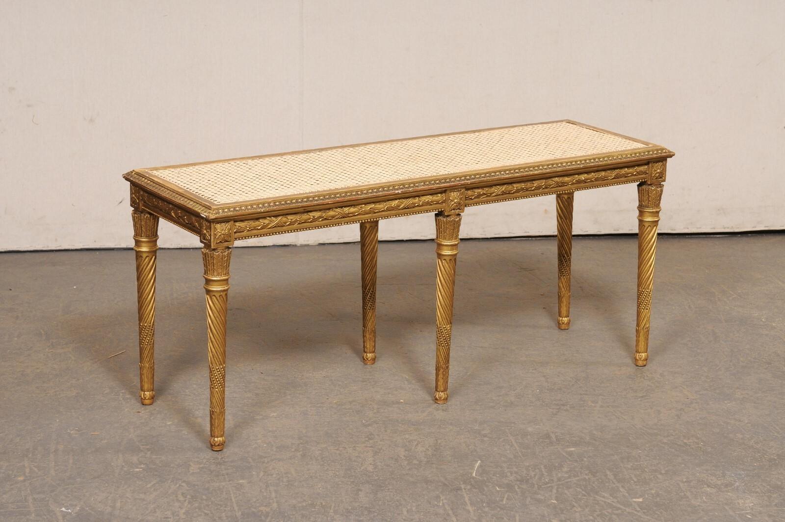 Banc français en bois sculpté et doré avec assise en rotin du début du 20e siècle. Ce banc ancien sans dossier originaire de France présente une assise cannée à la main, placée dans un cadre en bois accentué par une garniture en langue d'agneau sur
