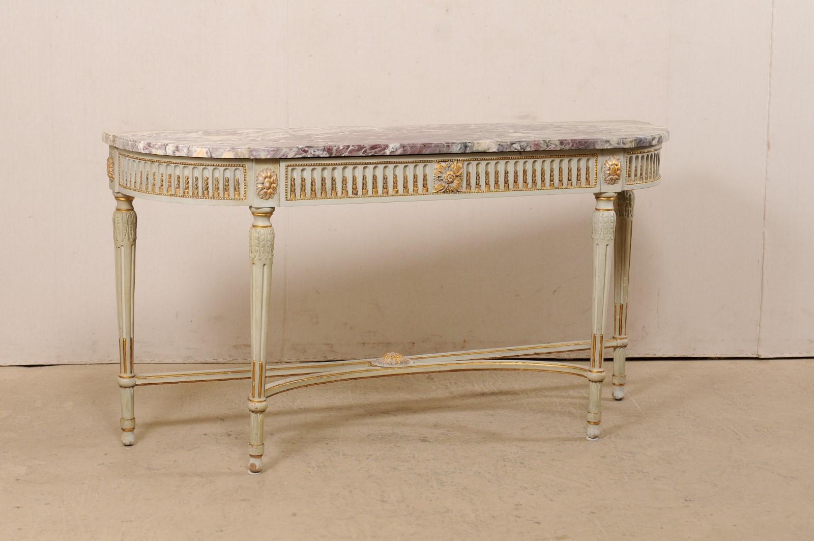 A lovely French marble top console table, with carved and gilt accents, from the turn of the 18th and 19th century. This antique table from France features an oblong shaped top with flattened backside and curved and stepped out shaped front. The