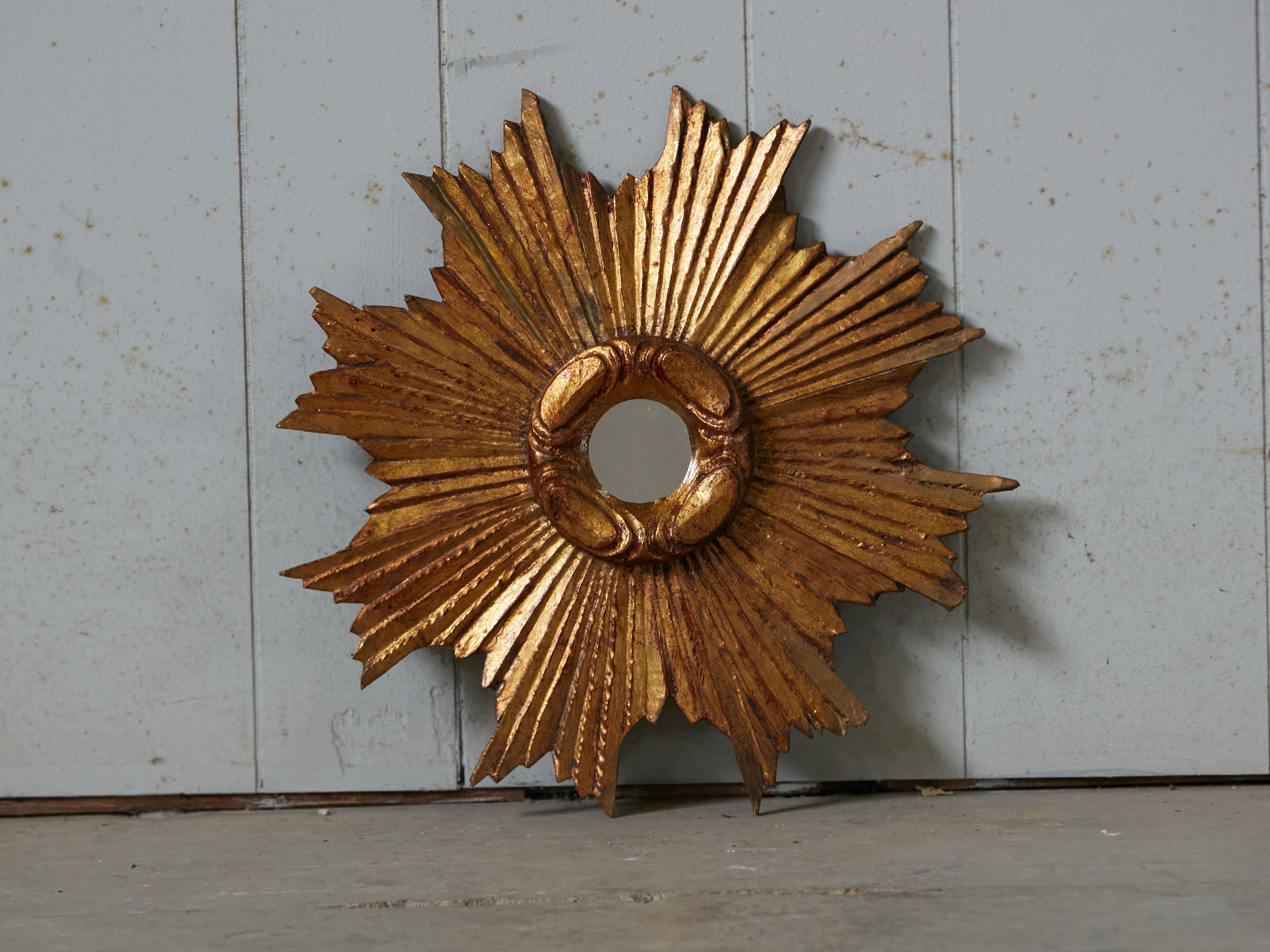 A French vintage carved giltwood sunburst from the early 20th century, with rays of varying sizes and cloudy frame. Created in France during second quarter of the 20th century, this sunburst features a giltwood frame showcasing rays of varying