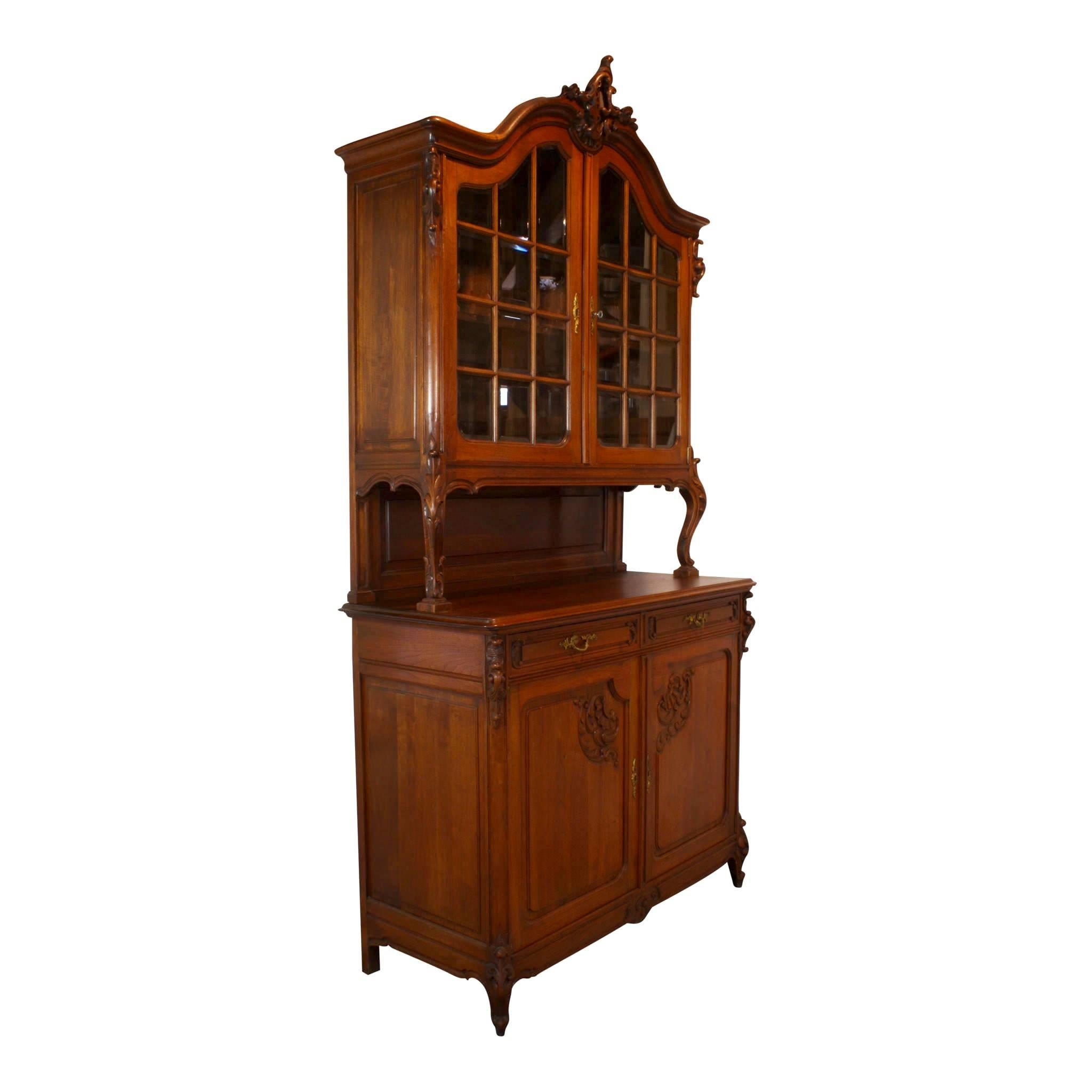 An arched cornice culminates in a beautifully foliated design incorporating flowers and ruffles with scrolled leaves atop this walnut china buffet. The arched, double doors with 24 beveled, glass panes in the upper gallery open to a fixed shelf. The