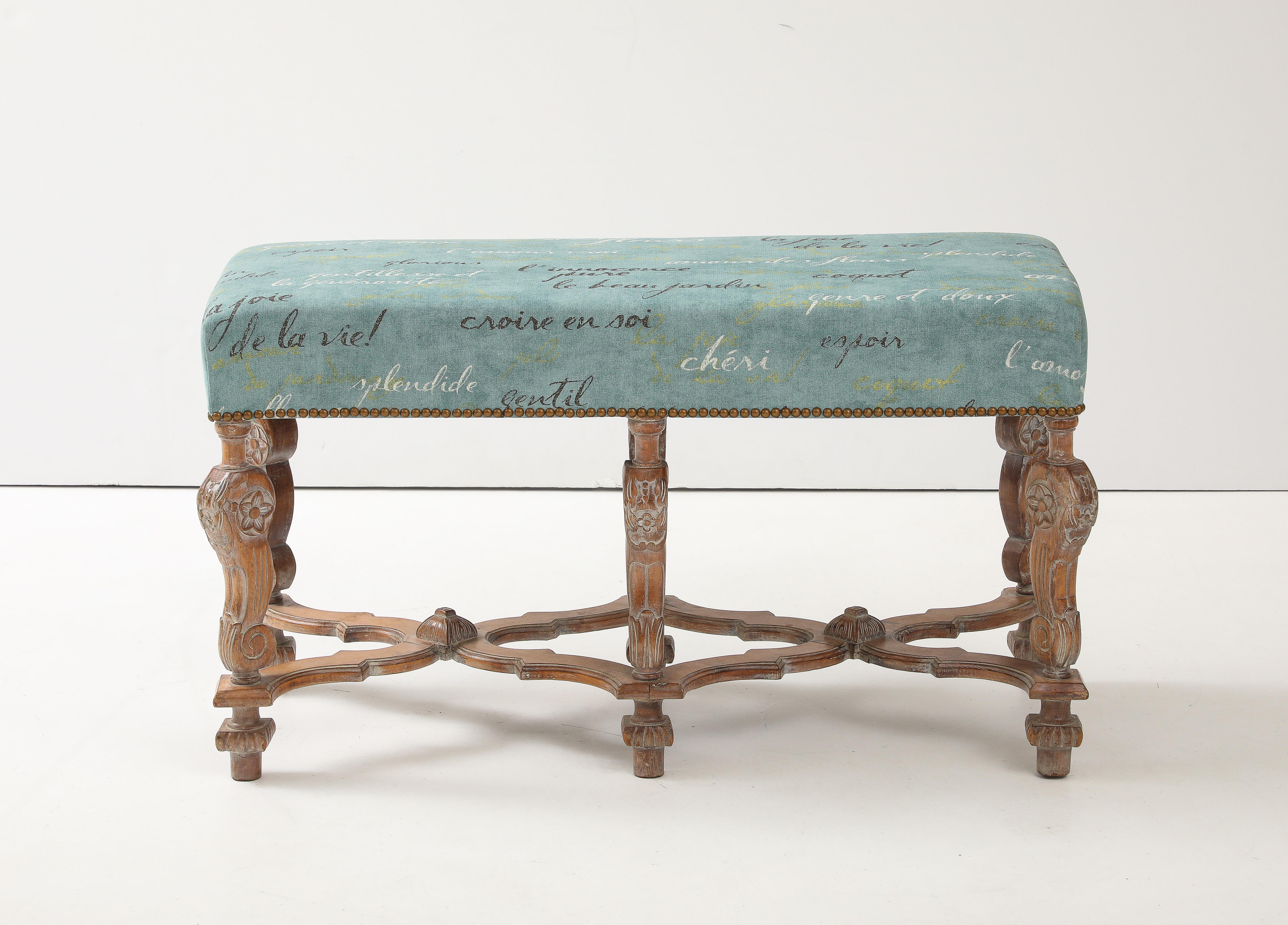 Banc en chêne sculpté de style provincial français du milieu du siècle, supportant un siège nouvellement rembourré avec des mots français fantaisistes imprimés sur le coton/lin. Têtes de clous en laiton vieilli sur le pourtour.