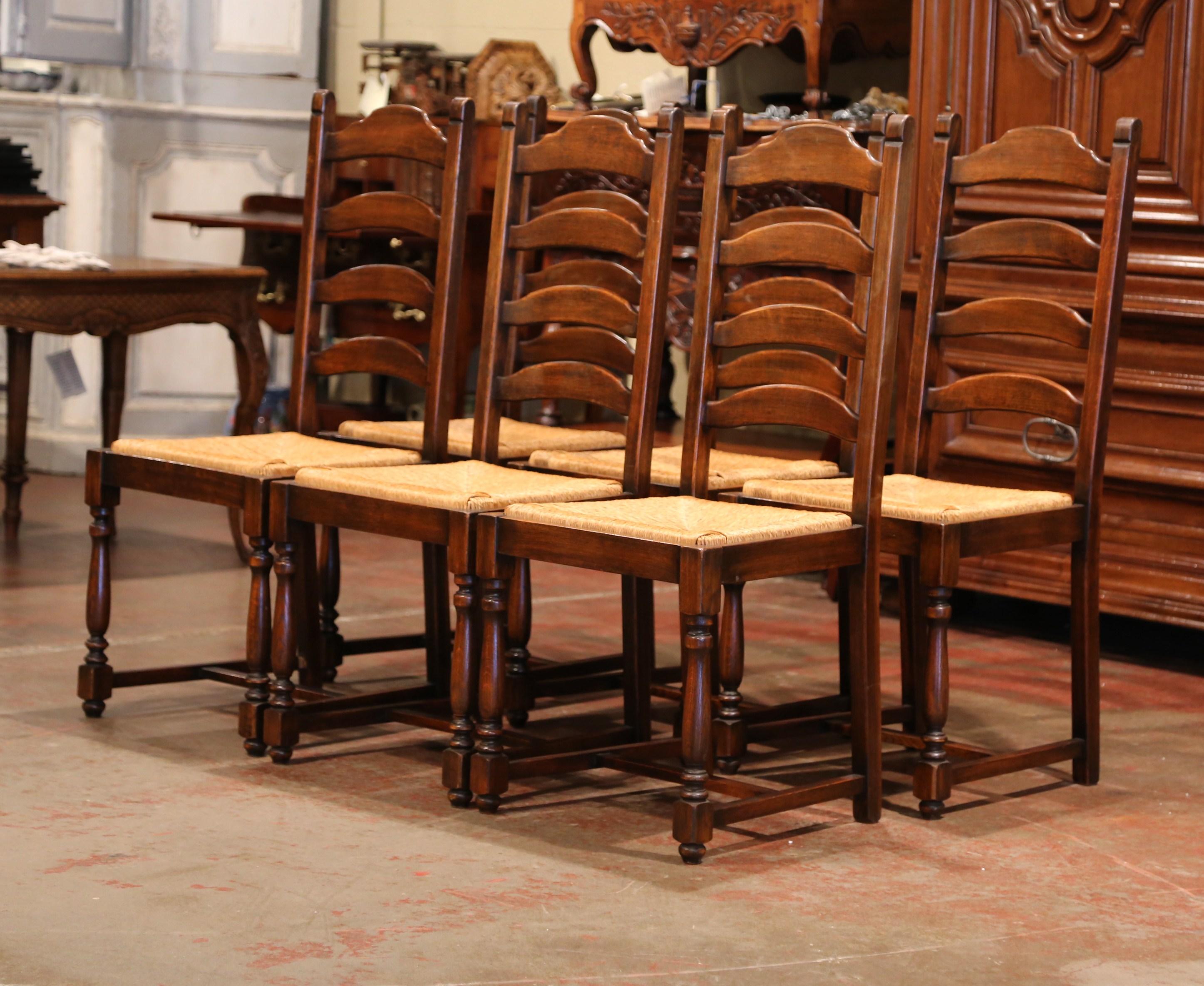 This elegant set of country chairs was crafted in France, circa 1990. Carved from solid oak, each chair has a tall back with four ladders across and two top finials. The seats have a woven rush surface, four carved, turned legs, and a pitched back,
