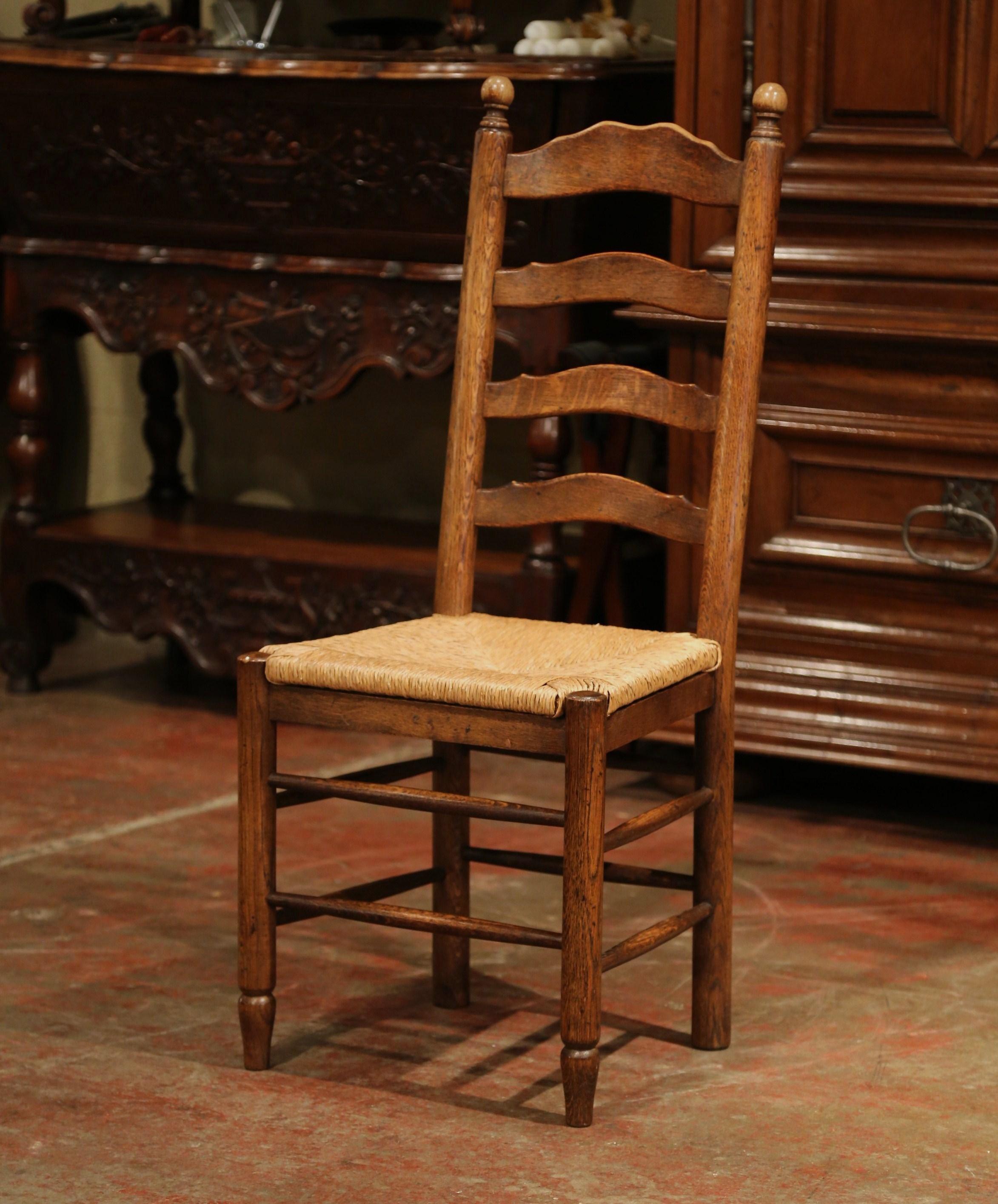 This elegant set of six country chairs was crafted in France, circa 1990. Carved from solid oak, each chair has a tall back with four ladders across and two top finials. The seat has woven rush surface, four carved, turned legs, and a pitched back,