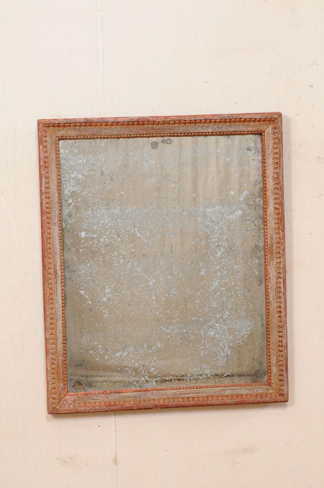 A French carved and painted wood wall mirror from the early 19th century. This antique mirror from France features a molded wood frame, which is nicely carved with decorative trim and petite raised beading along the inner surround. The piece has a