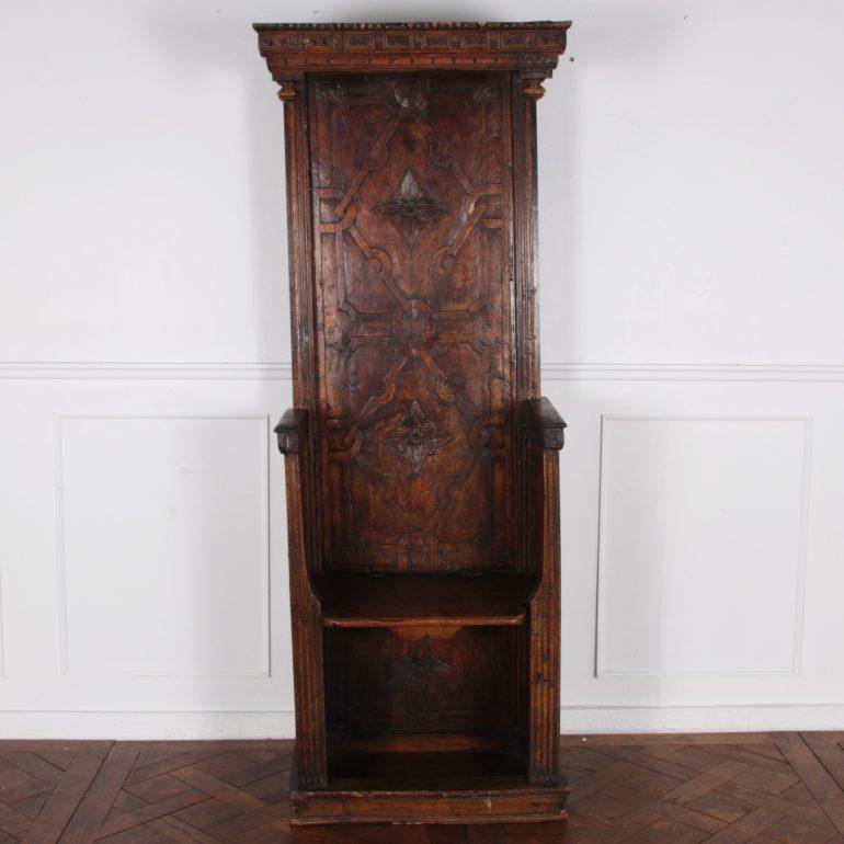 An unusual French ‘Bishop’s Throne’ in walnut, with carved details to the paneled sides, back, and top, the arms with fluted pilasters and the crown with elaborate and fine carving.

The seat lifts up to allow for standing, and has a carved-face
