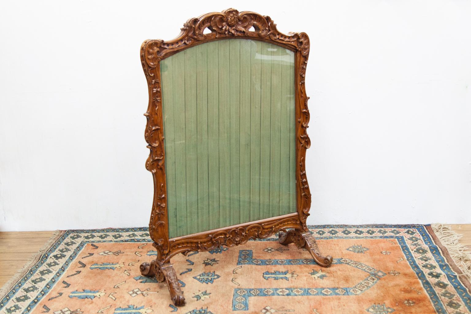 French carved walnut firescreen, with green pleated fabric. It is elaborately carved in high relief on the front and back. Only the front has a glass cover.