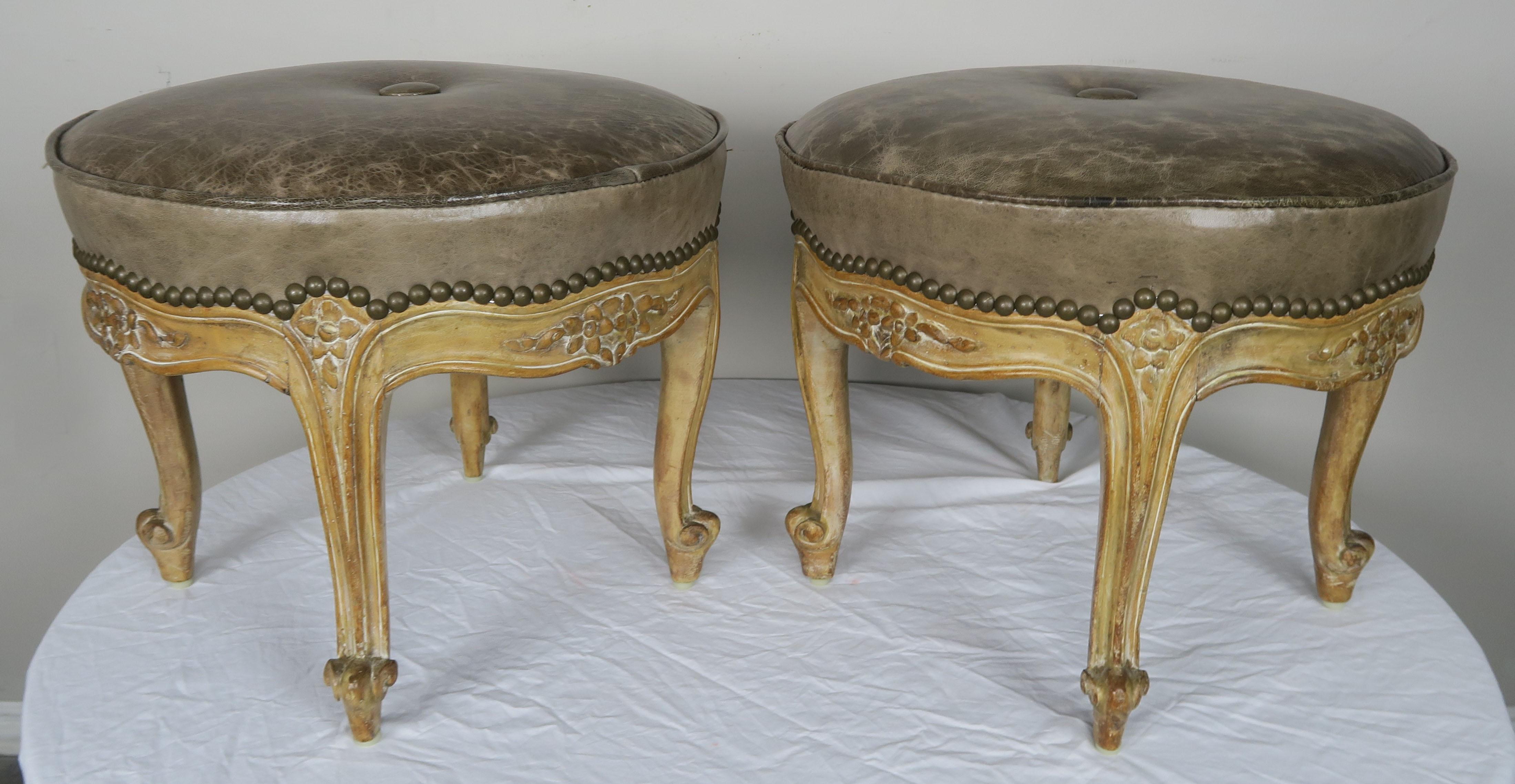 Pair of French carved walnut Louis XV style stools in a natural walnut finish with petite carved flowers on the top of legs and on frame of stools. The stools stand on four cabriole legs that end in ram's head feet. Upholstered in distressed leather