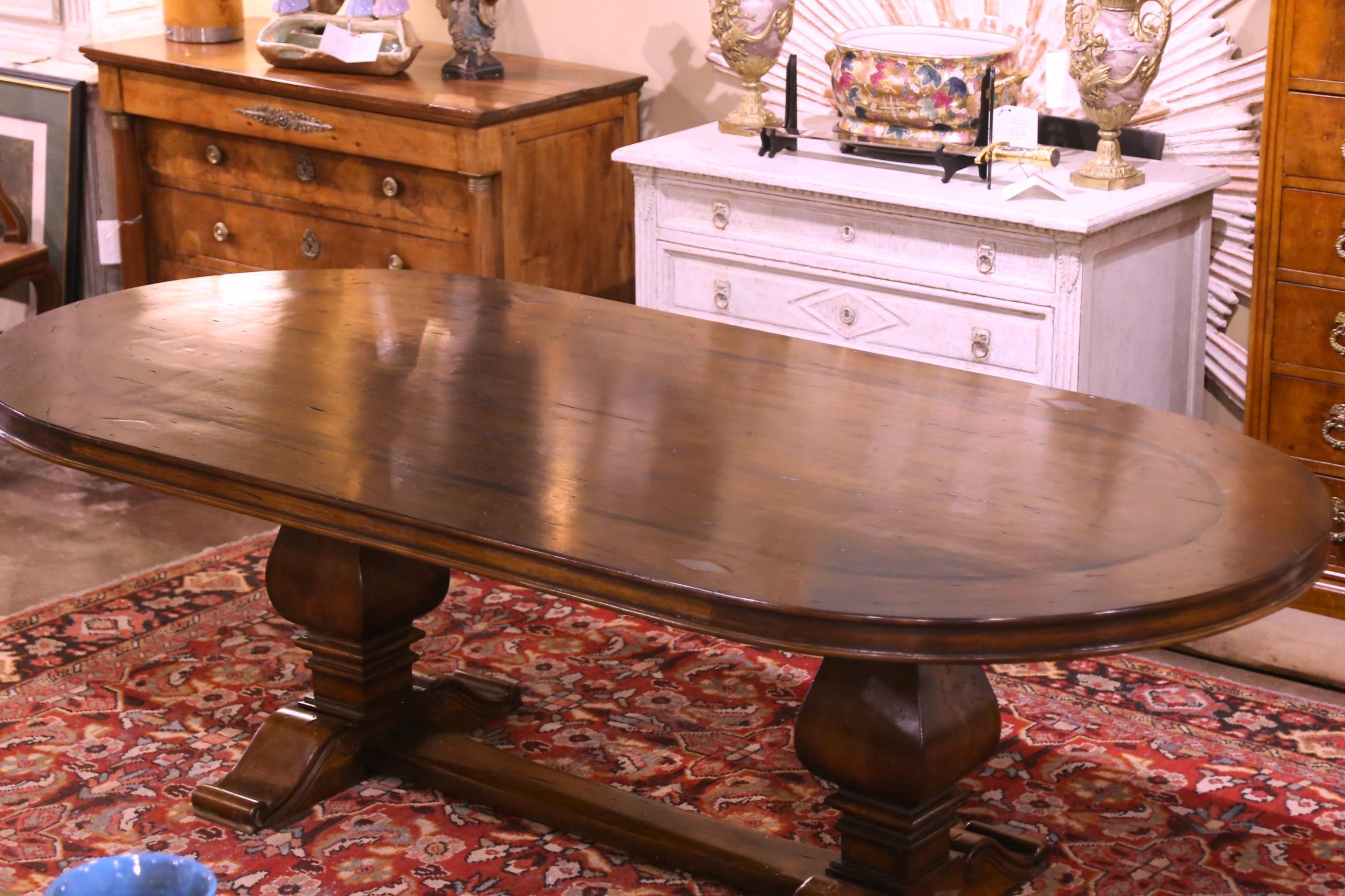 This elegant and large oval dining room table was crafted using old antique timbers, and followed an 18th century design from the Pyrenees of France. Built of solid walnut, the table sits on a trestle base, supported with a pair of hand carved
