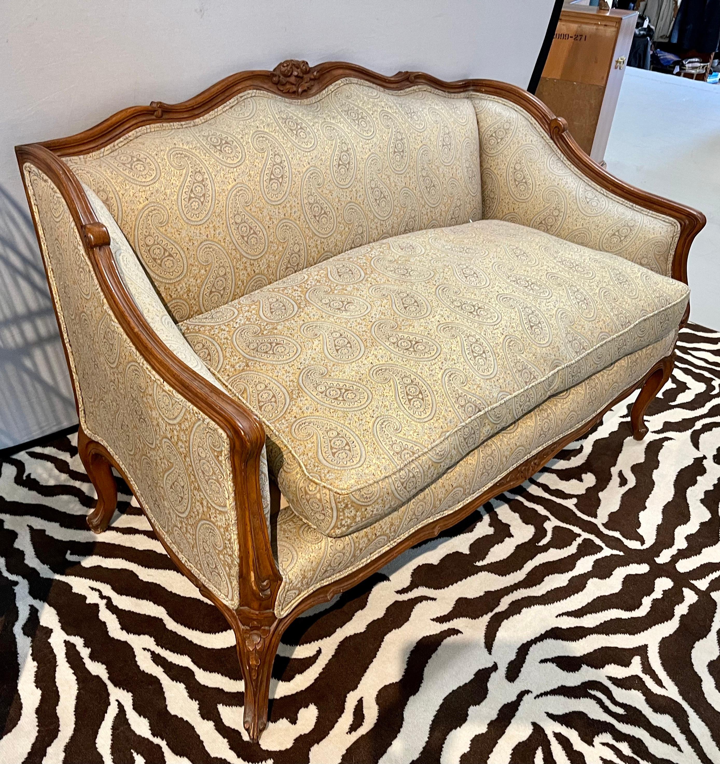 Elegant 1970's walnut settee with luxurious subtle paisley fabric. The fabric is still in fine shape and cold be original. Sits very well and everything is sturdy as it should be. Features rich carved detail in the walnut. Own the best.