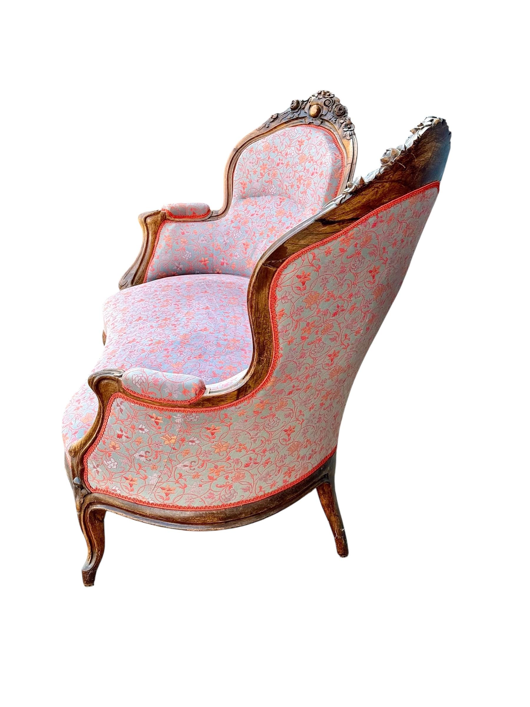 Questo eccezionale divano antico francese è un esempio straordinario di artigianato del XIX secolo, caratterizzato da una struttura in noce splendidamente scolpita e da una silhouette elegante con schienale rialzato a doppia estremità. Il design è