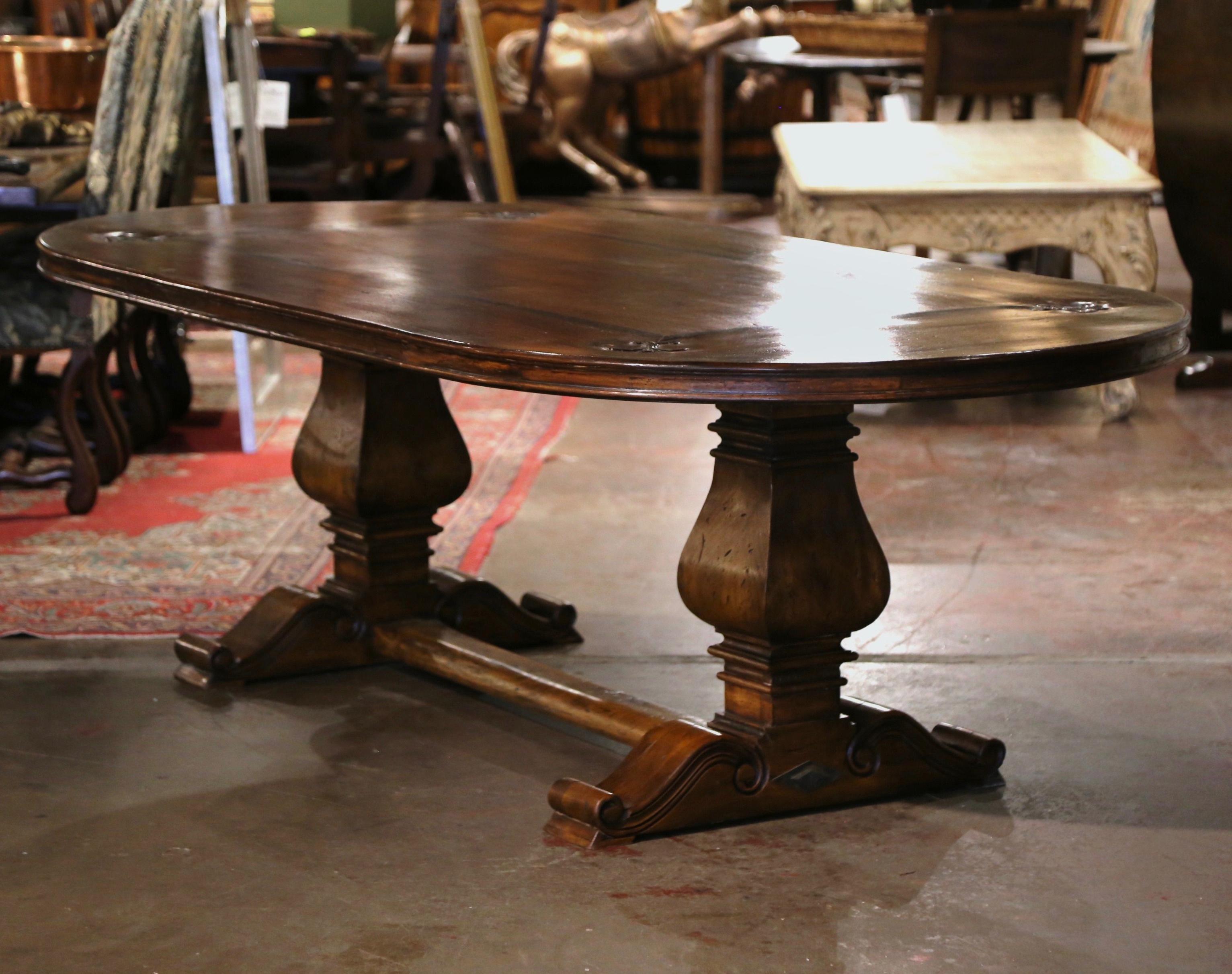 This elegant eight foot oval walnut dining room table was crafted using antique timbers, and followed an 18th century design from the Pyrenees of France. The table sits on a trestle base, supported by a pair of hand carved 