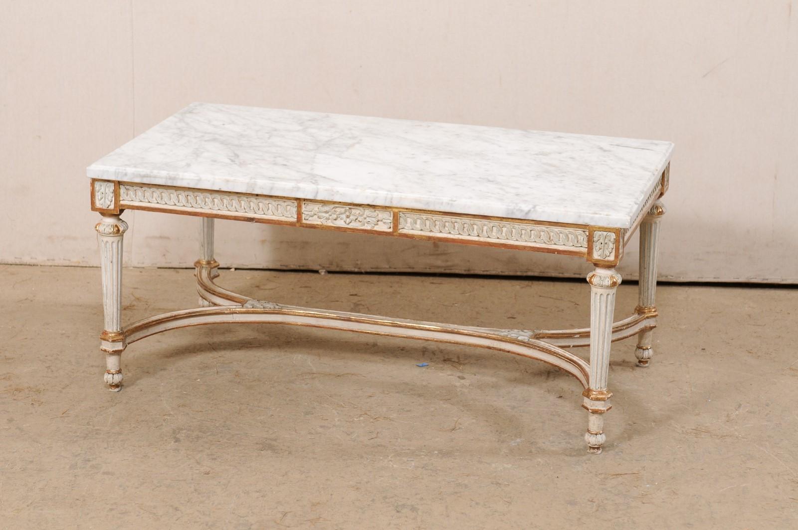 A French carved and painted wood coffee table with marble top from the mid 20th century. This vintage coffee table from France has a rectangular-shaped marble top (white with gray veining) which rests upon a wooden base with apron carved in a