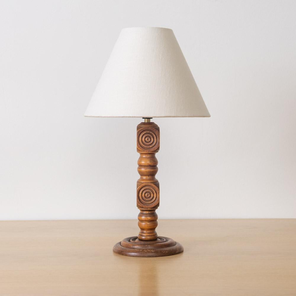Bellissima lampada da tavolo intagliata di Charles Dudouyt, Francia, anni '40. Stelo in legno intagliato a mano con design a cerchio su una base rotonda. Nuova tonalità di lino affusolata e nuovo cablaggio. La finitura originale del legno mostra una