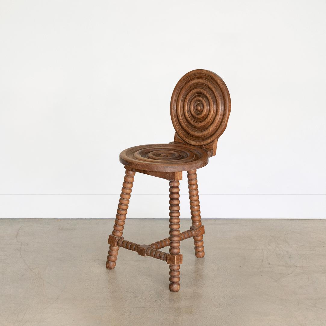 Incredible French 1940's carved wood chairs in the style of Charles Dudouyt. Beautiful circular carved wood back and seat with ring detailing and bobbin wood tripod legs. Original dark wood finish. Two available, sold individually.