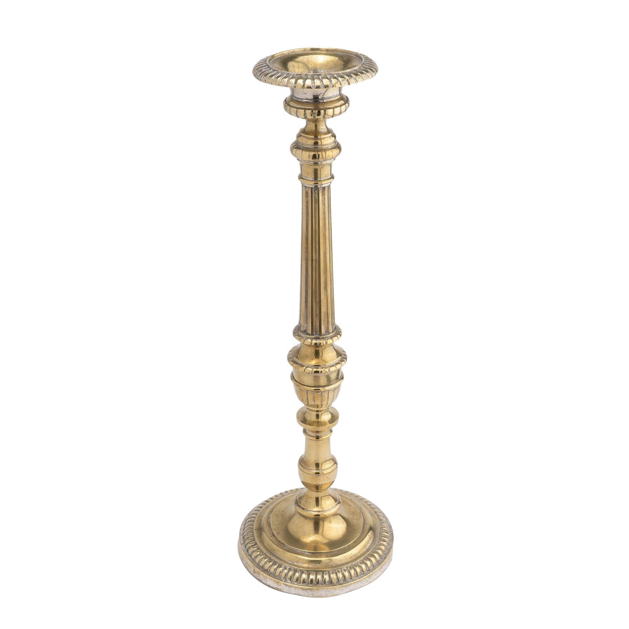 Core cast brass altar candlestick with traces of original silvering. The design features a calyx urn form candle cup on a fluted column over two variations of urn form turnings, threaded to a domed circular base with beaded edge.

France, circa