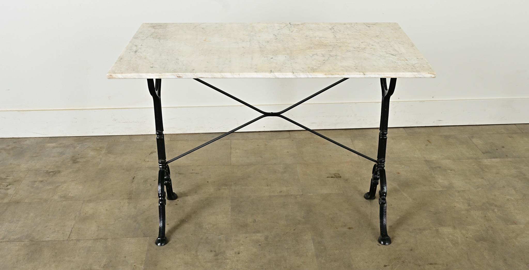 Une table de bistrot française classique avec un plateau en marbre blanc sur une base en fonte noire. La pierre naturelle a une finition lisse, adoucie et est plate sur les bords. Les gravures et les piqûres sur le marbre correspondent à l'âge et au