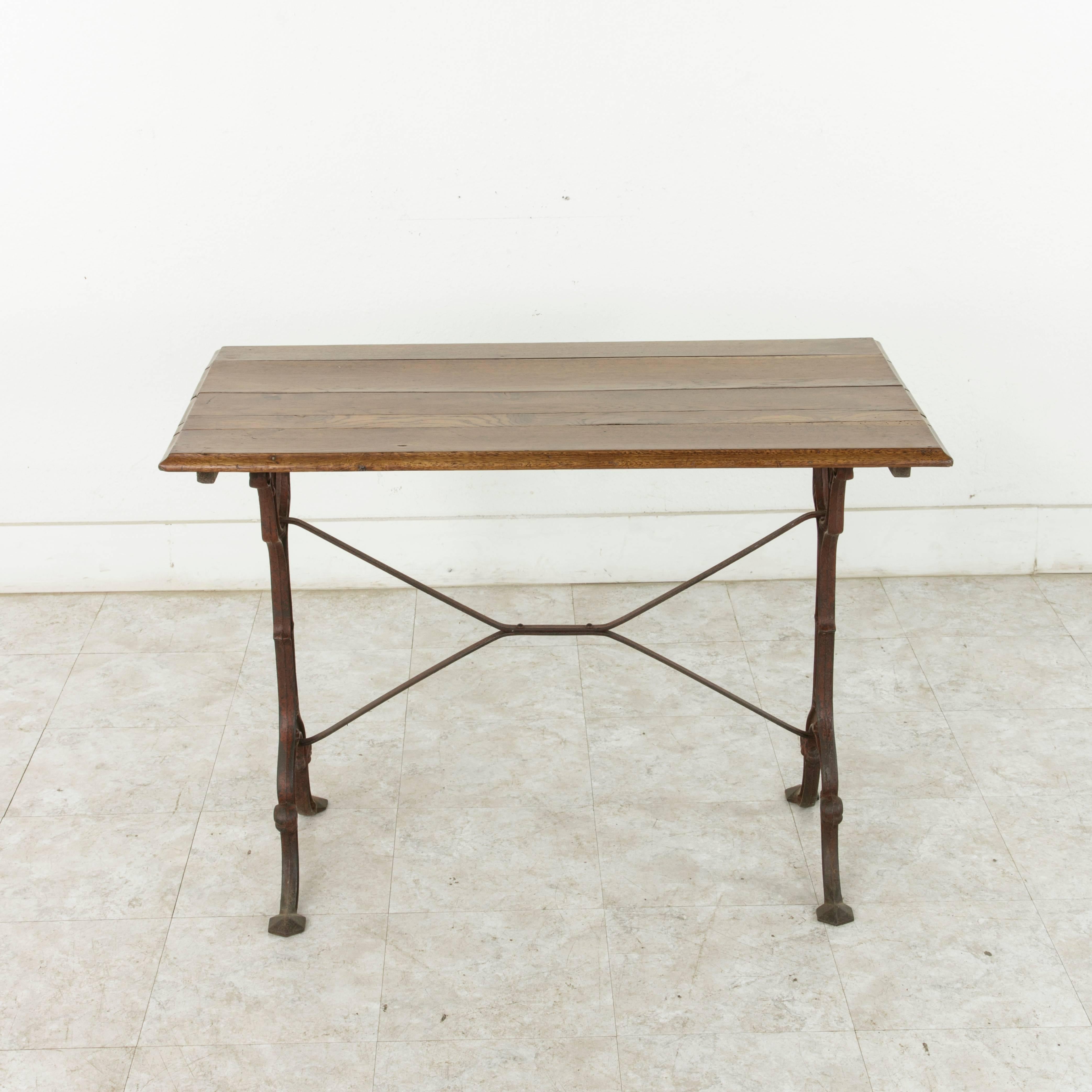 Originally used in a French brasserie around the turn of the 20th century, this bistro table or cafe table features a cast iron base and a beveled oak top. Classic scrolled iron legs are joined by an X-stretcher that provides additional stability to
