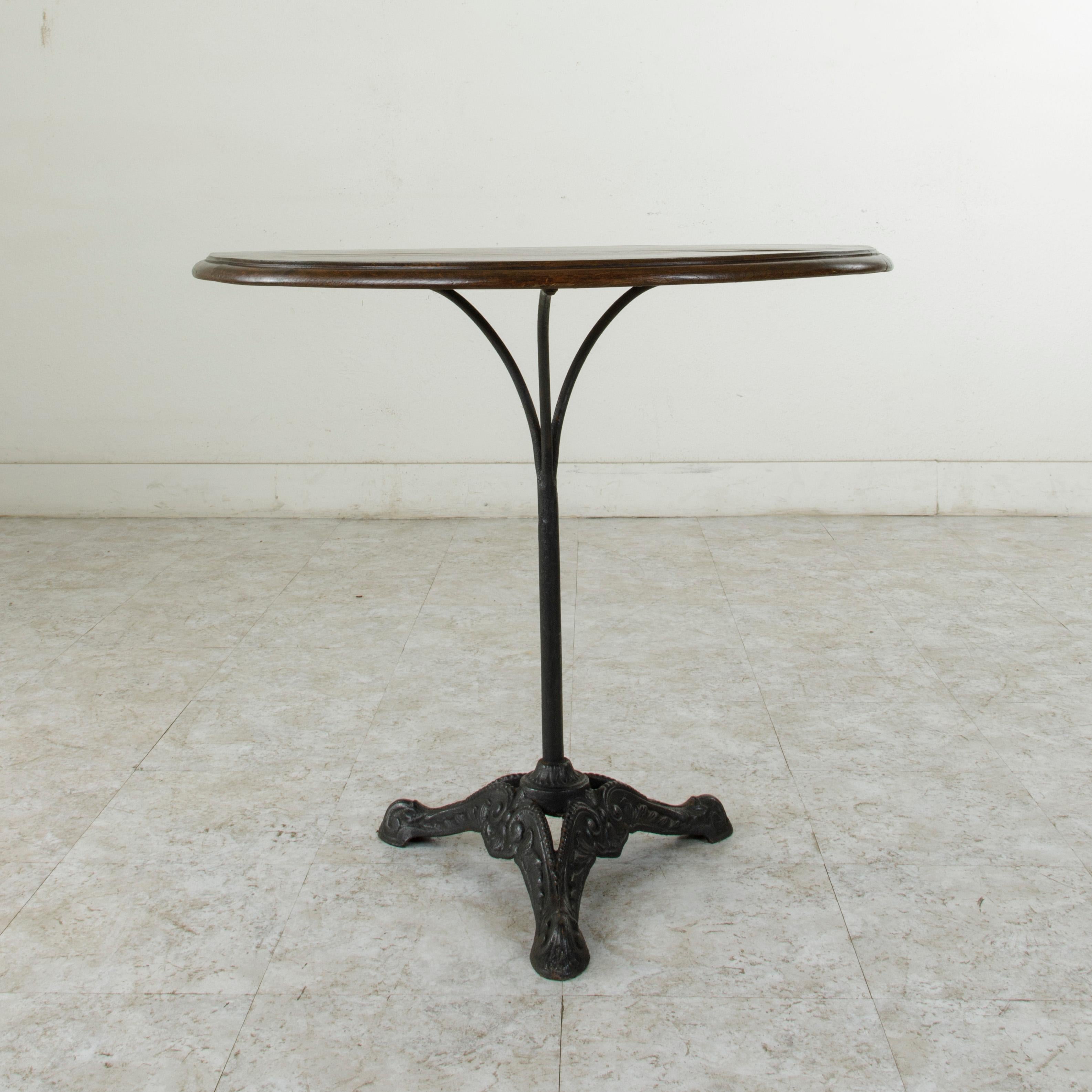 This turn of the 20th century French bistro table or cafe table features a cast iron pedestal base and a 31-inch diameter beveled walnut top. Three arms support the top and join to the central column. The pedestal rests on three feet detailed with