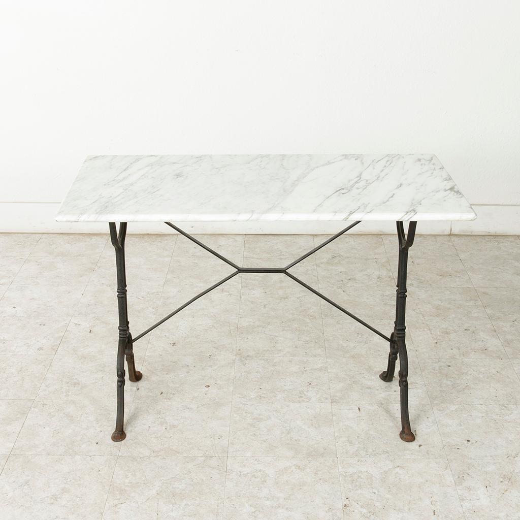 Originally used in a French brasserie around the turn of the twentieth century, this cast iron bistro table or cafe table features a solid white marble top with grey veining. Classic scrolled iron legs support the top and are joined by an