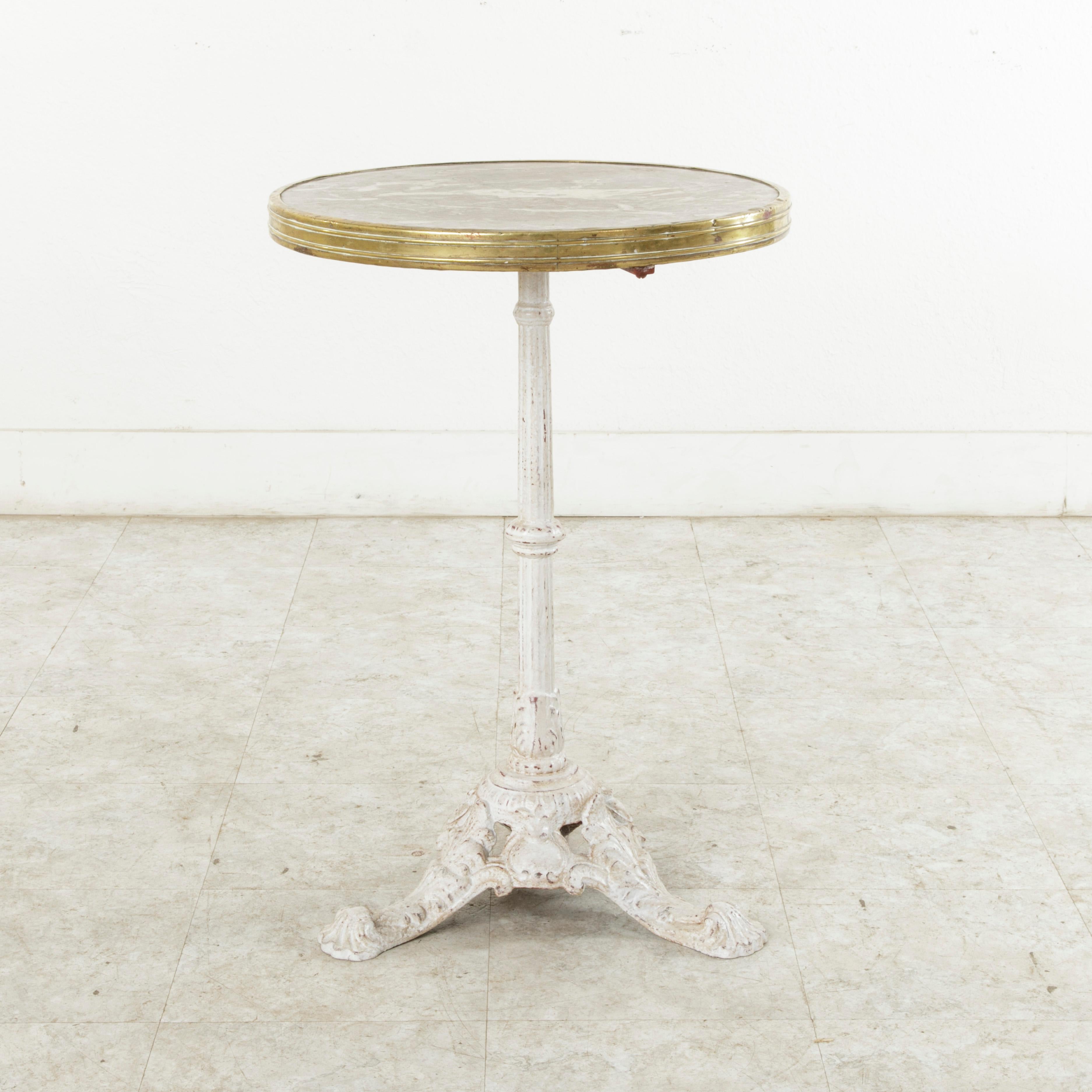 This French cast iron bistro table from the turn of the twentieth century features a grey and rose colored marble top with white veining surrounded by a brass rim. Its top rests on a central pillar supported by a tripod base. The painted iron base