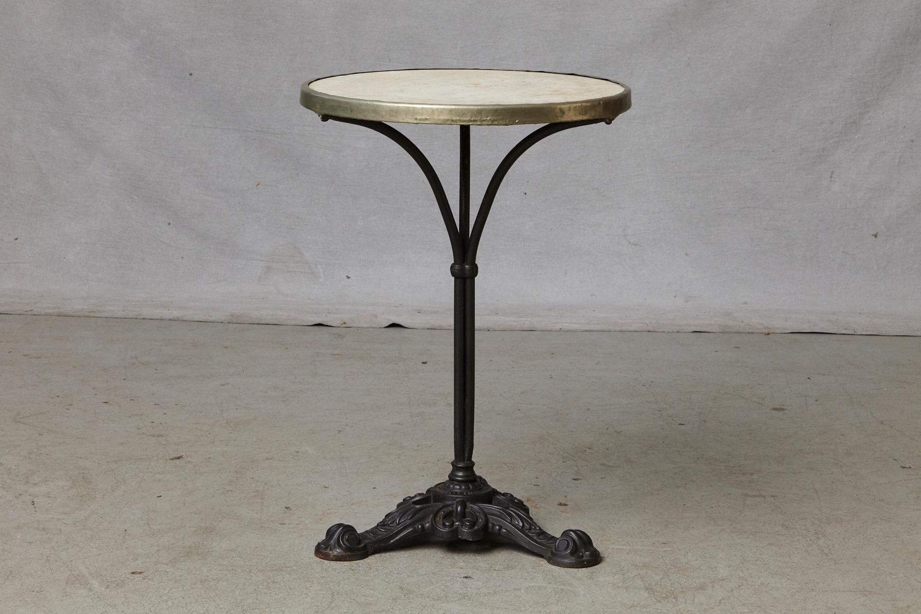 Antique French Bistro table, marble top with original brass rim mounted on a black painted cast iron tripod base, circa 1920s. The maker's mark E. Nautre Paris is stamped in the base of the table.
The table has a fantastic patina with typical signs