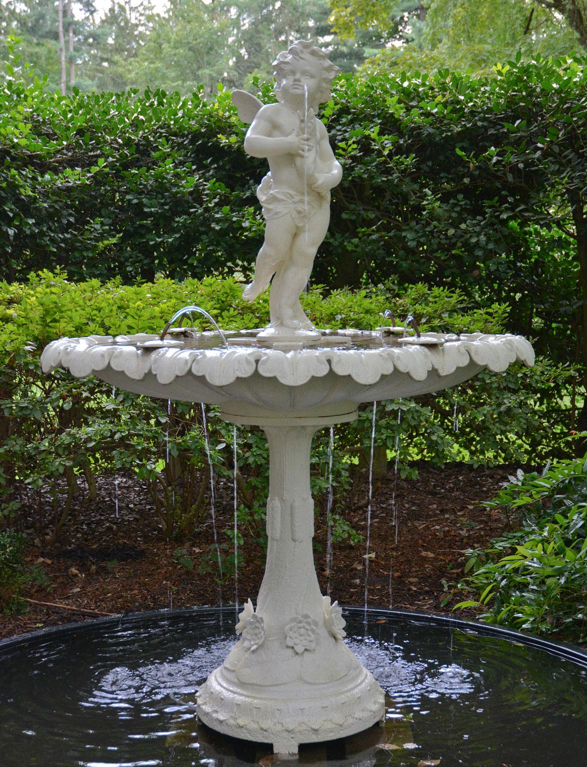 A cast-iron fountain figure of a winged cherub with upturned countenance and windblown hair, standing on his proper left leg, with right leg swept back, and holding a fish in his hands, the fish plumbed for water, French, circa 1870, the base marked
