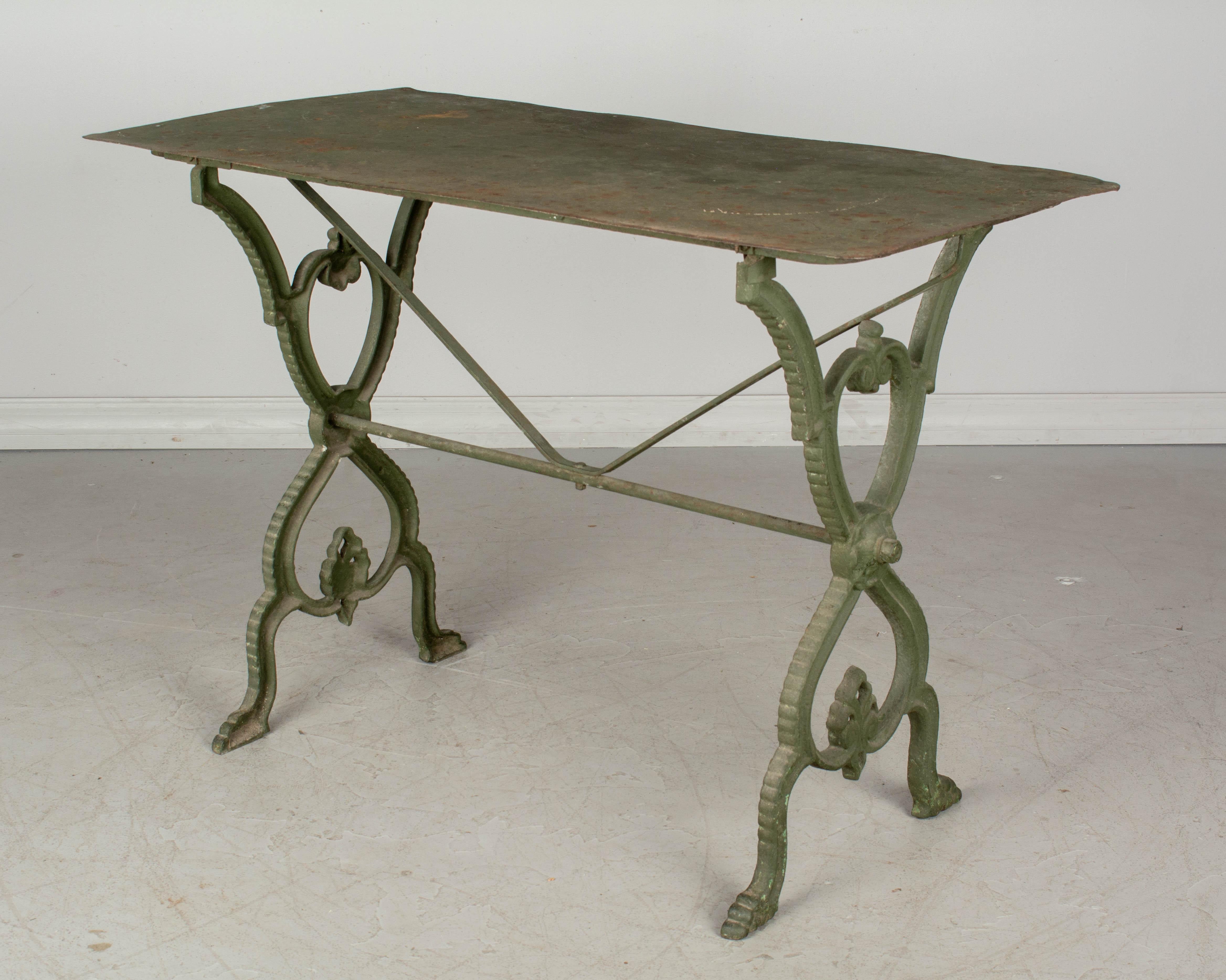 A French cast iron garden bistro table with old verdigris painted finish. Tole top with weathered rusty patina. Good quality casting with decorative Fleur de Lis form at the base. Perfect for outdoor use. Please refer to photos for more details. 
  