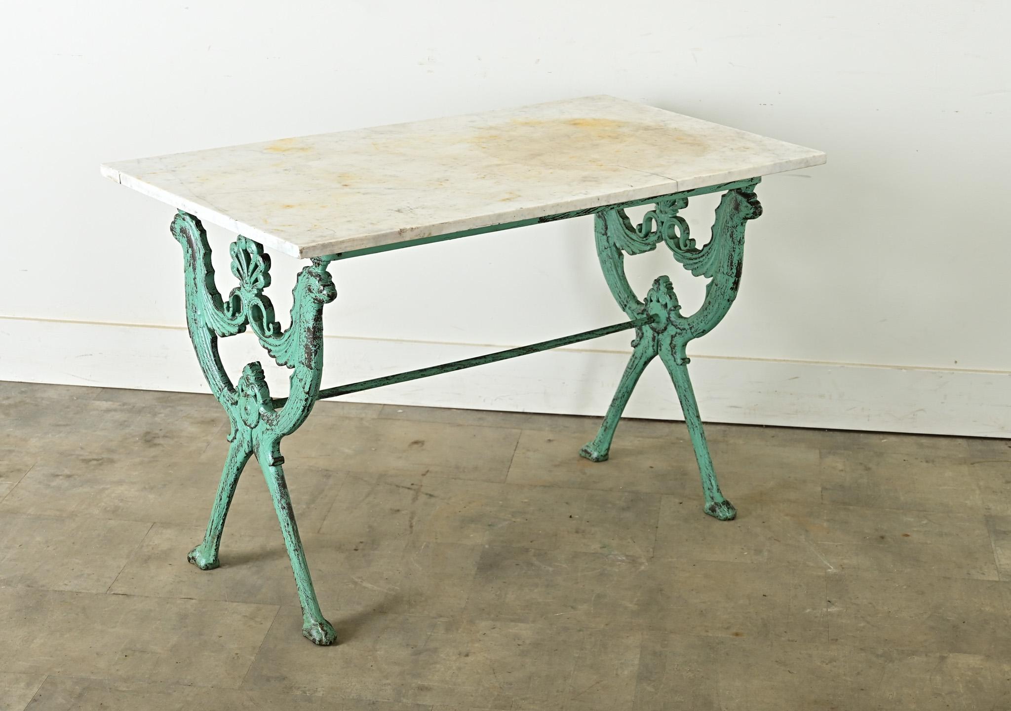 This mid-19th century French marble-topped bistro table, circa 1860-1880, borrows from the heraldic devices of the Habsburg Empire by referencing their double-headed eagle with crown motif in the cast iron table base to signify great power and