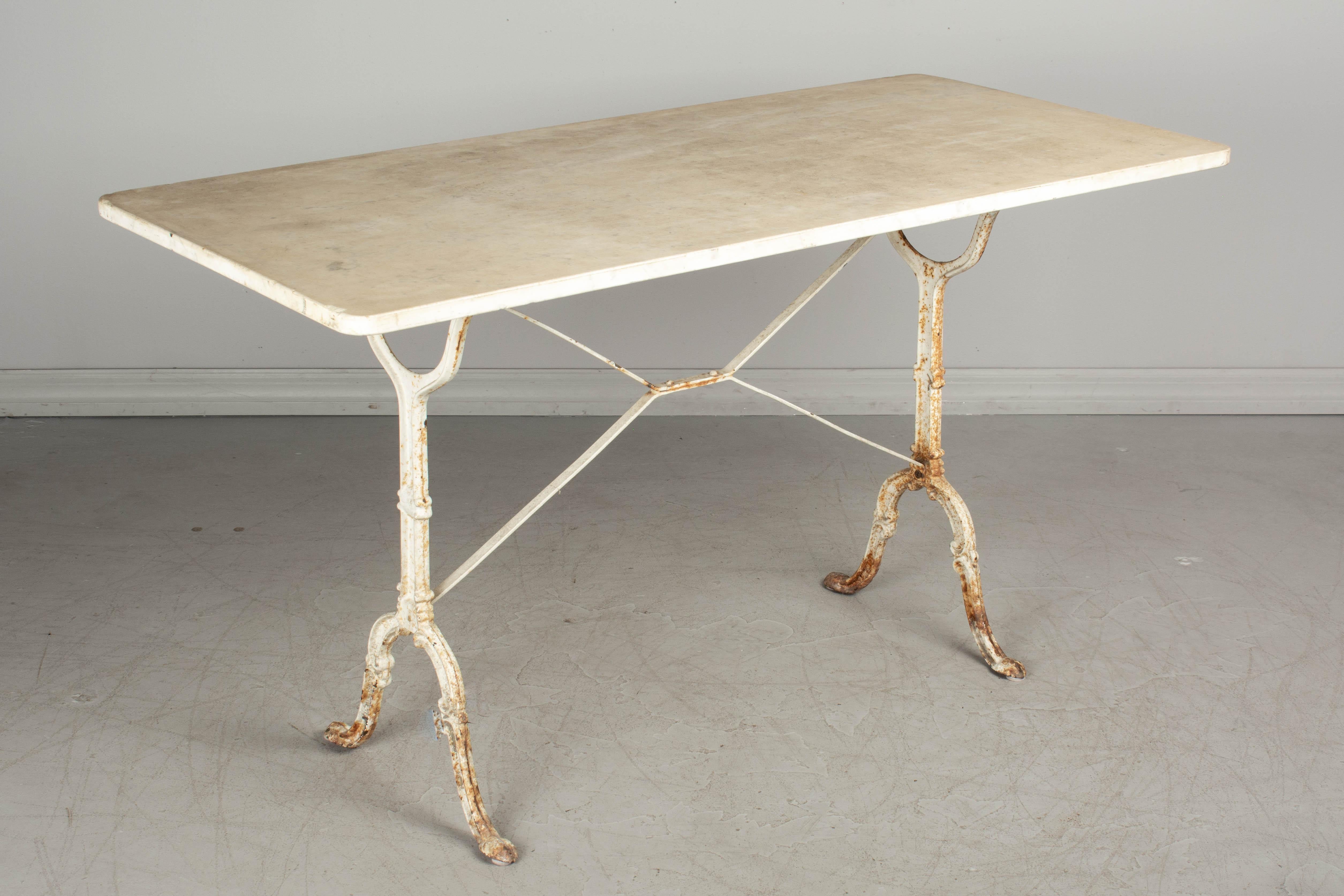 A French cast iron marble top bistro table. Base has old white painted finish with rusty patches. The large marble top is as found with the base and has a beautiful worn patina. Several chips to the edges of the marble. Perfect for outdoor.