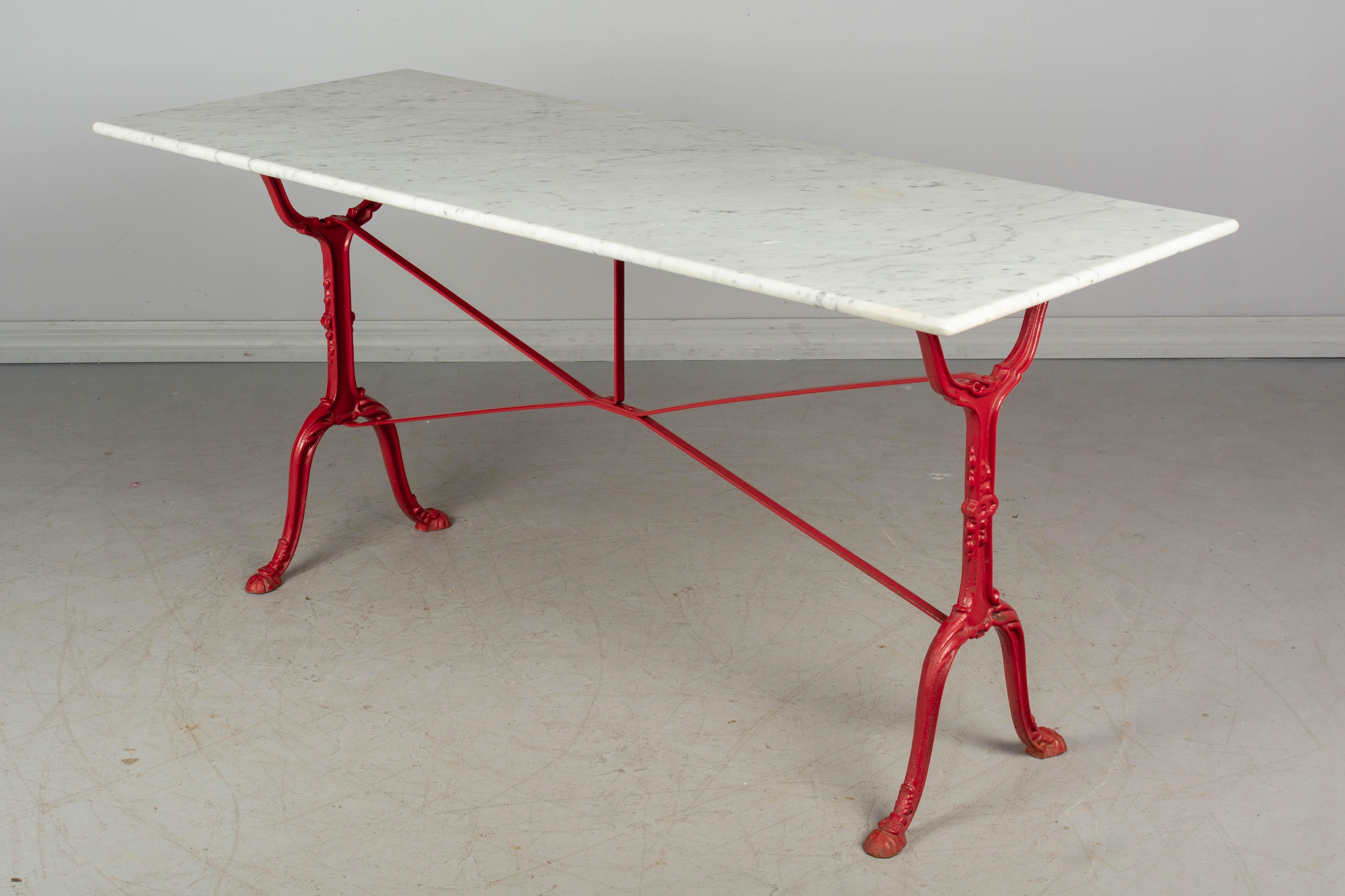 A French cast iron marble top bistro table. Base has bright red painted finish. Large white veined marble top is in good condition with minor wear. Perfect for outdoor use.
