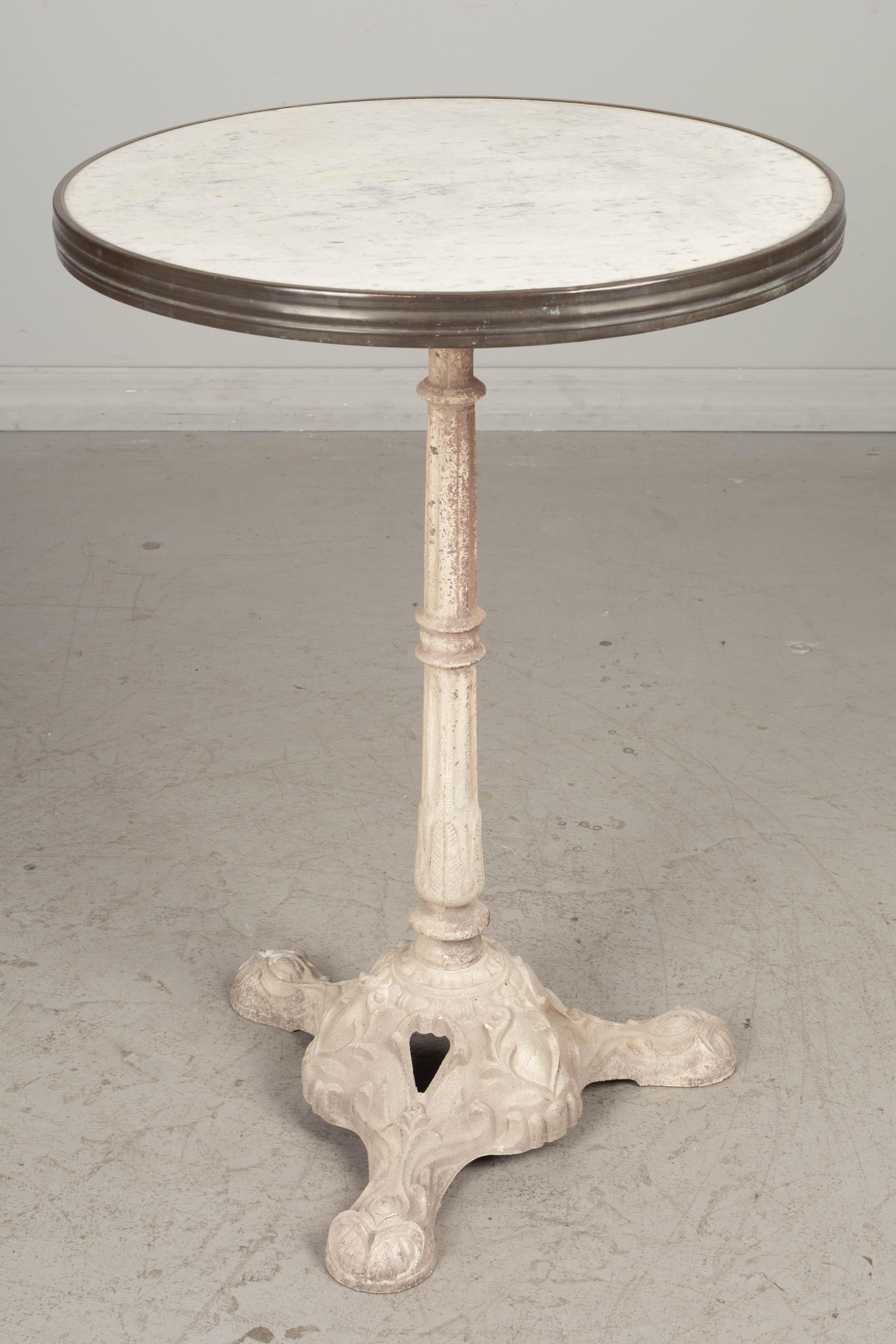 An early 20th century French cast iron bistro table with white painted pedestal base. Original marble top with brass band around the perimeter. Good quality heavy casting. Base was repainted as some point, circa 1900-1920. Dimensions: 28
