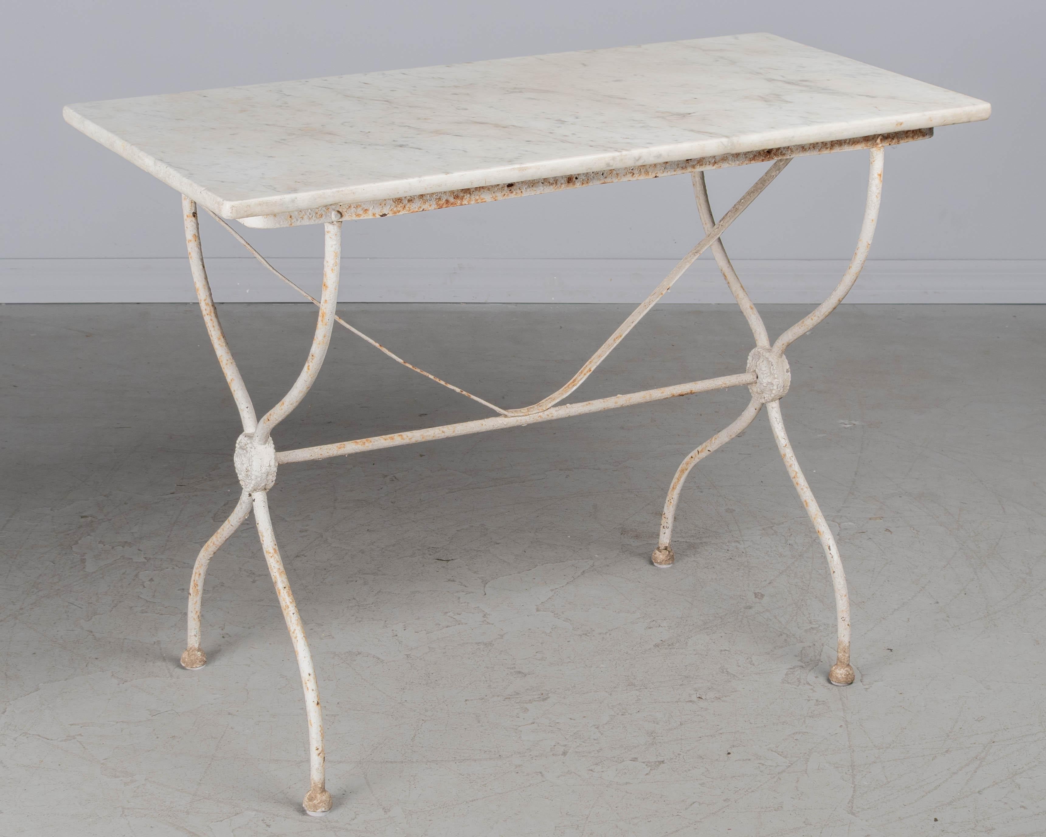 A French cast iron marble top bistro table with white painted patina. Base is sturdy and marble rests on top, unattached. Marble is old and not original to the base but fits perfectly. May be used indoors or as an outdoor garden table. Some flaking